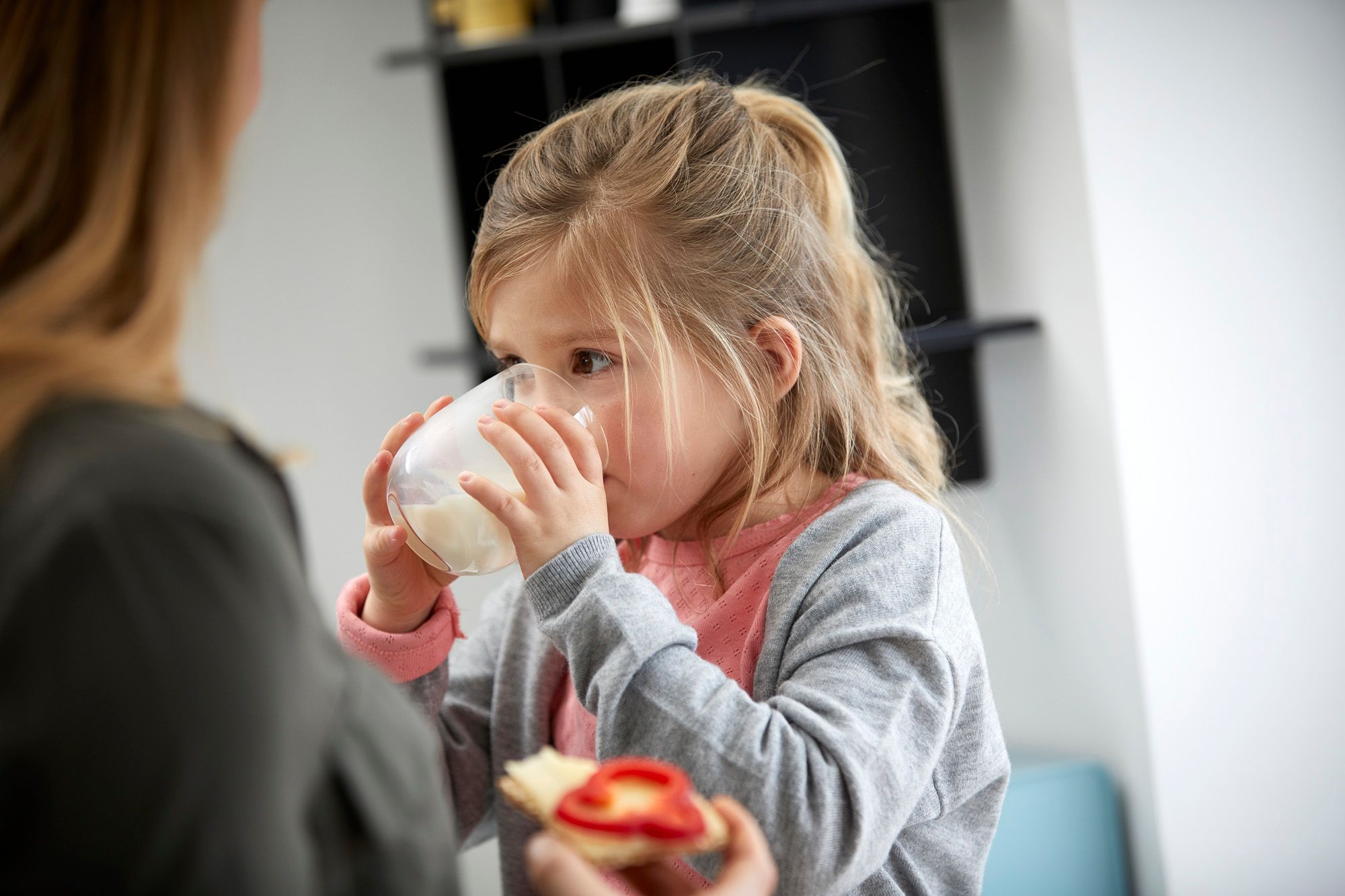 Mor med brødskive og ostepålegg og barn med melkeglass