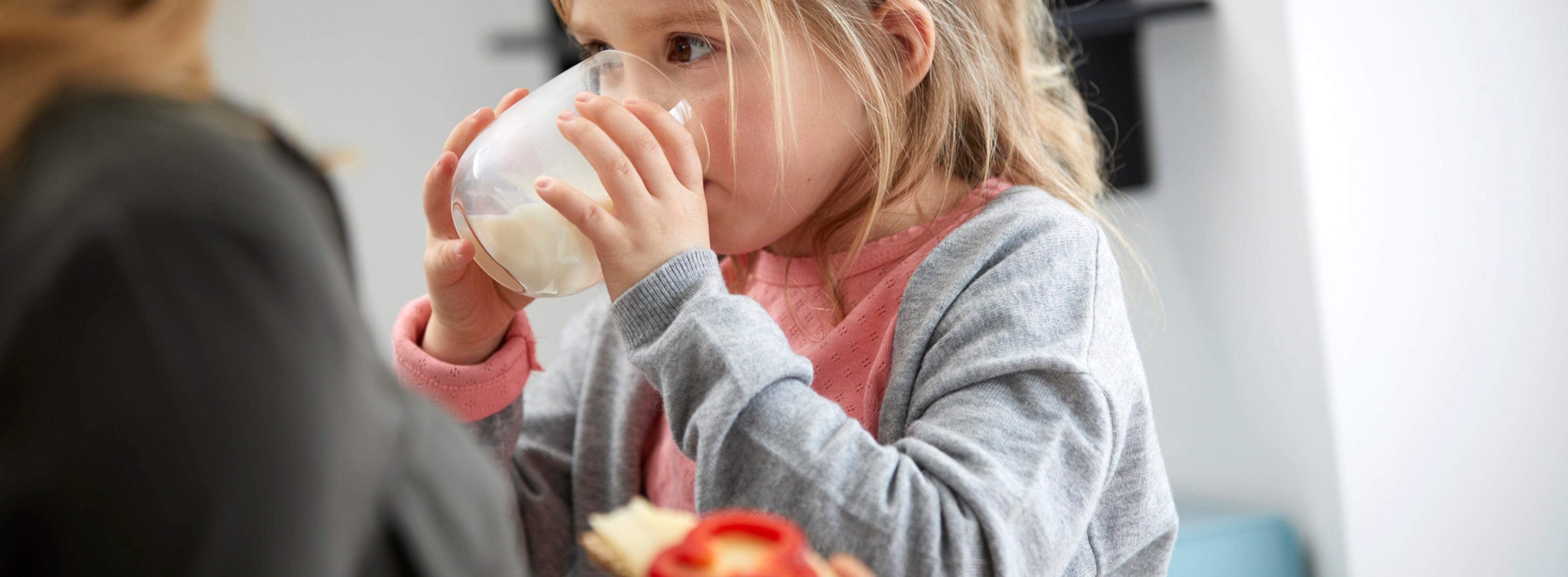Mor med brødskive og ostepålegg og barn med melkeglass