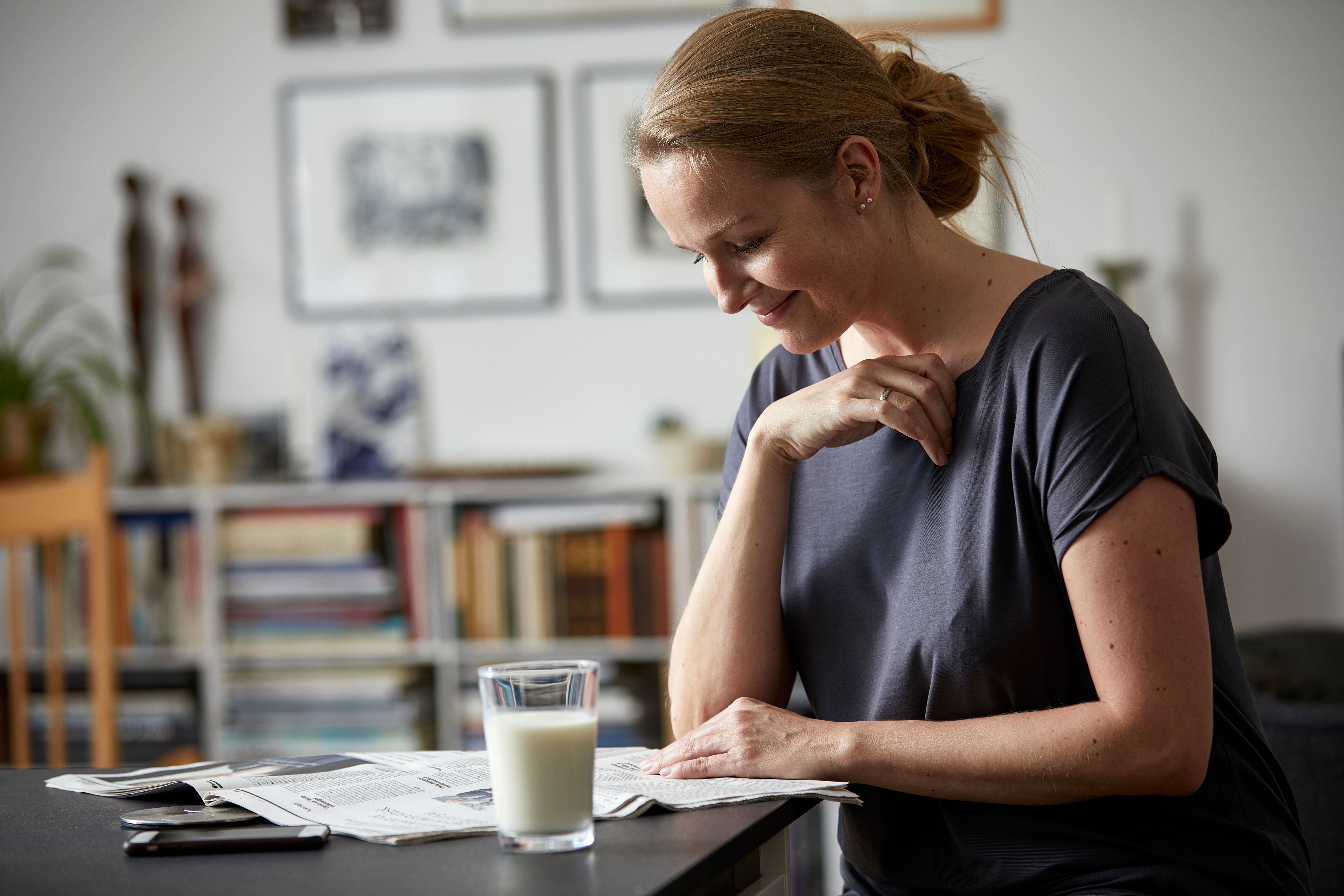 Kvinne som leser avisen. Et glass melk på bordet. 
