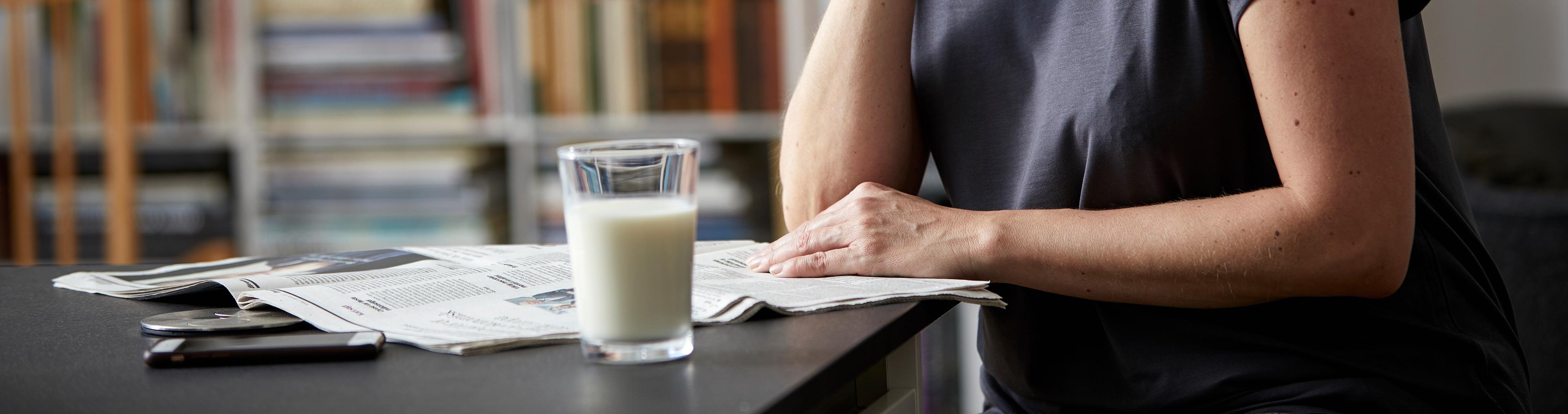 Kvinne som leser avisen. Et glass melk på bordet.
