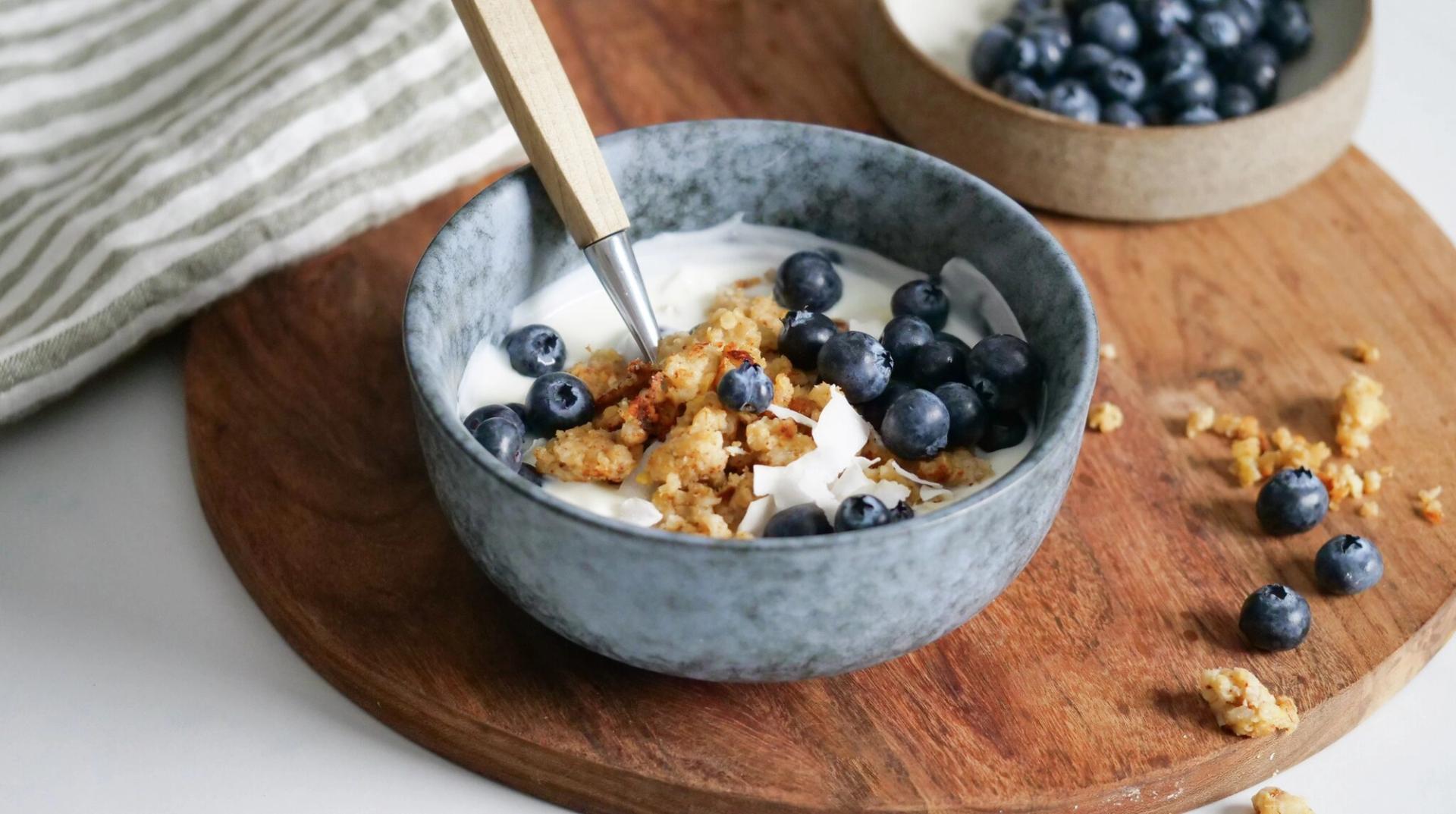 en bolle med yoghurt toppet med stekt havregrøt og blåbær