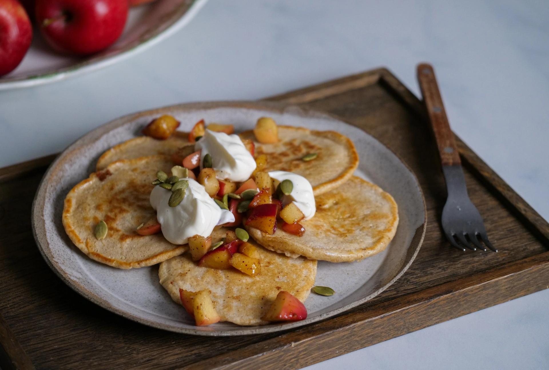A plate of pancakes topped with cooked apples, cream, and pumpkin seeds.