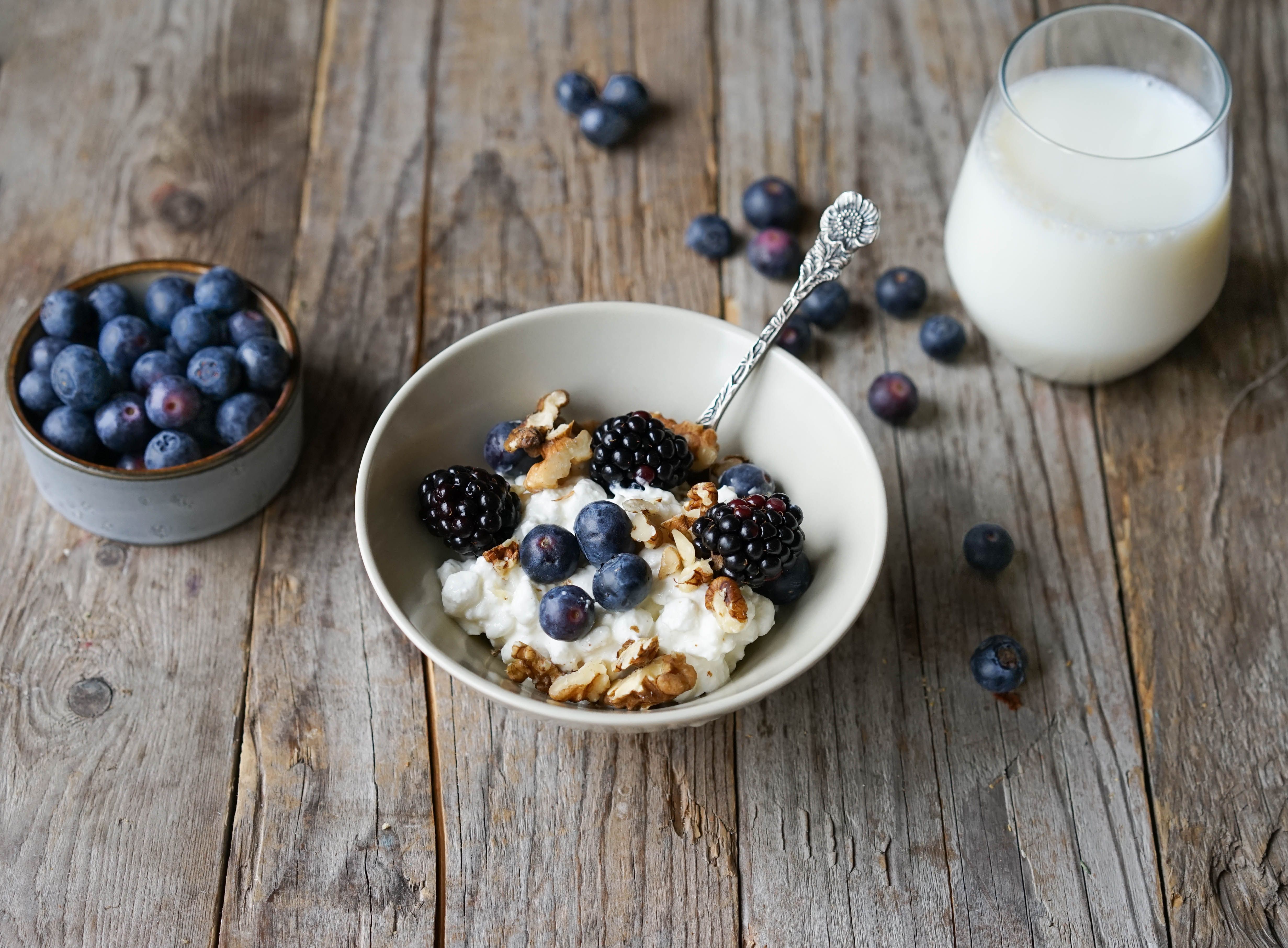 En skål med cottage cheese med blåbær og bjørnebær, et glass melk og en bolle med blåbær