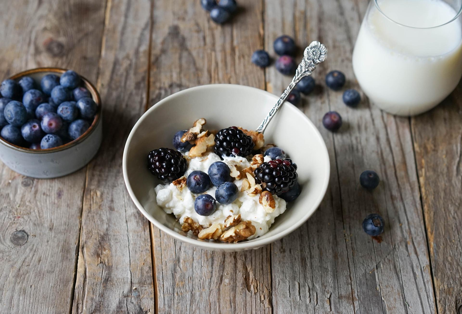 En skål med cottage cheese med blåbær og bjørnebær, et glass melk og en bolle med blåbær