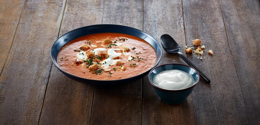 En skål med tomatsuppe med creme fraishe i, og en mindre skål med crème fraîche ved siden av 