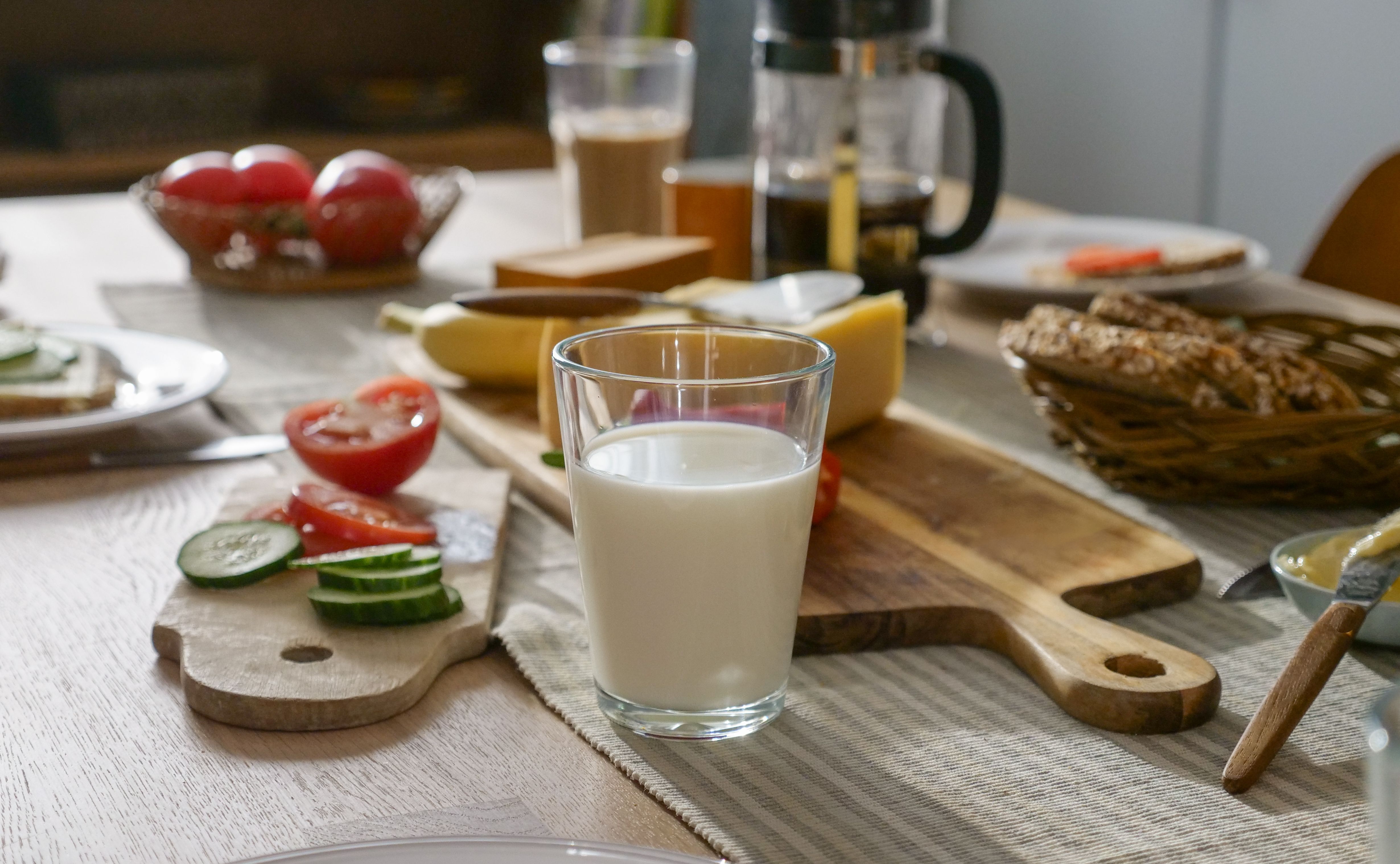 a glass of milk is sitting on a wooden table next to a cutting board with vegetables .