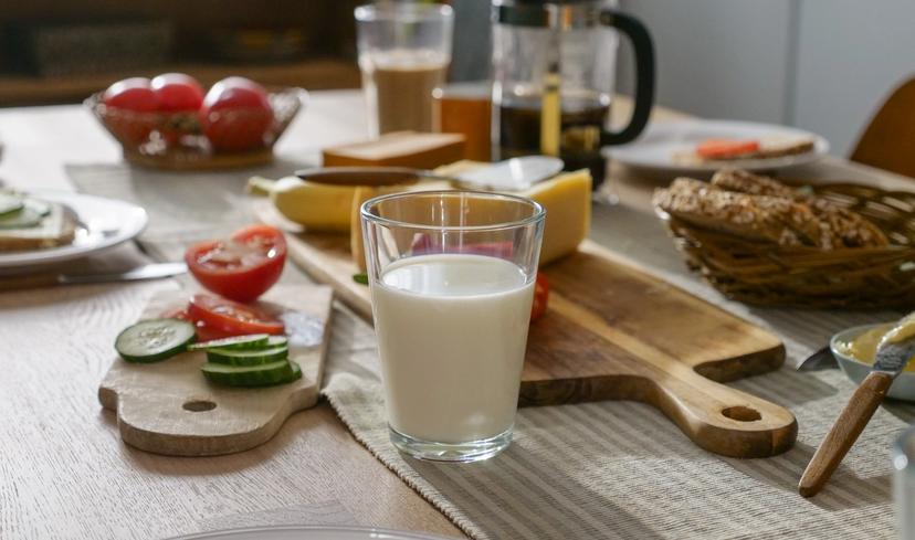 a glass of milk is sitting on a wooden table next to a cutting board with vegetables .