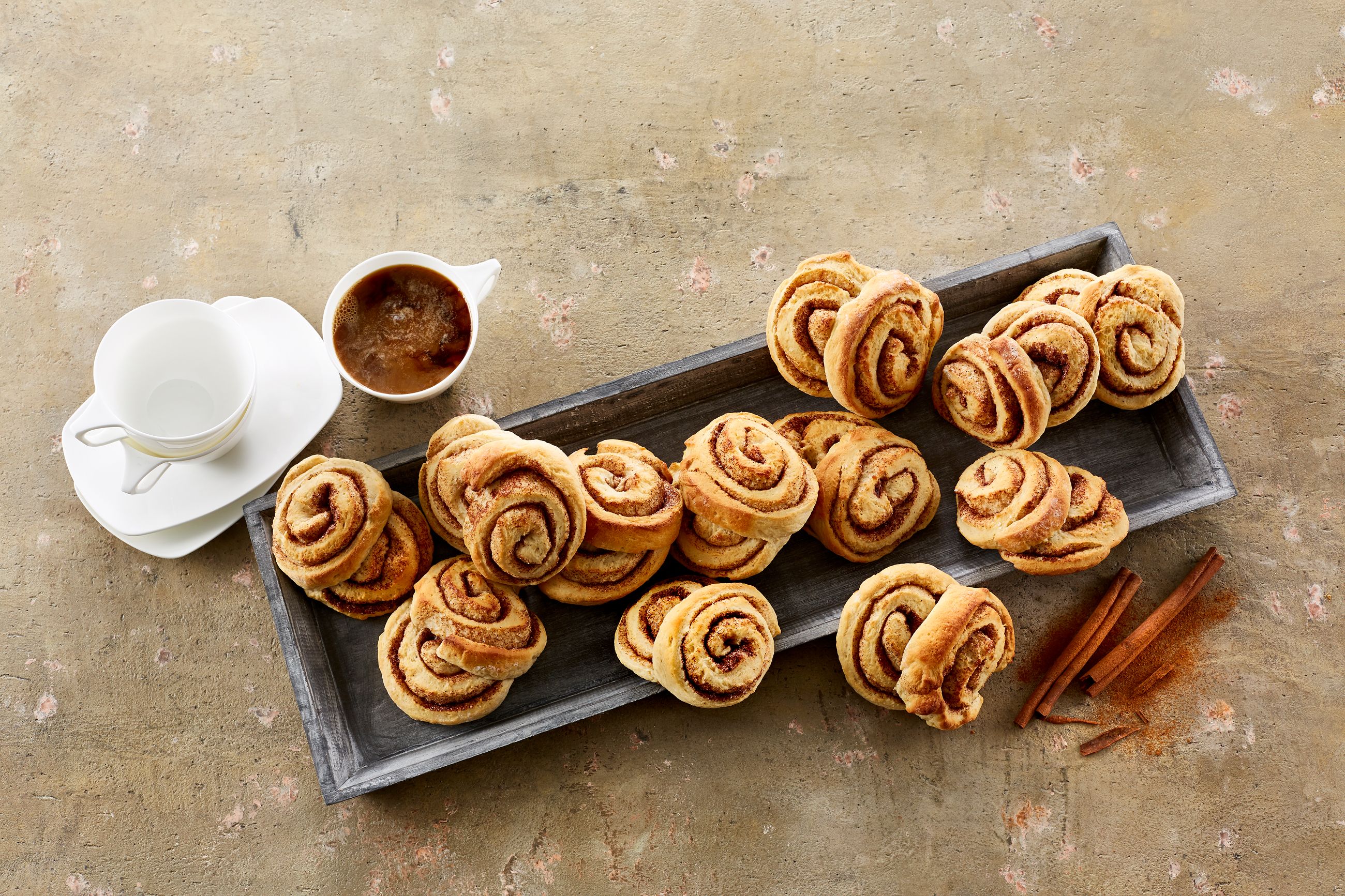Kanelboller med kvarg på et fat ved siden av en kopp kaffe med melk