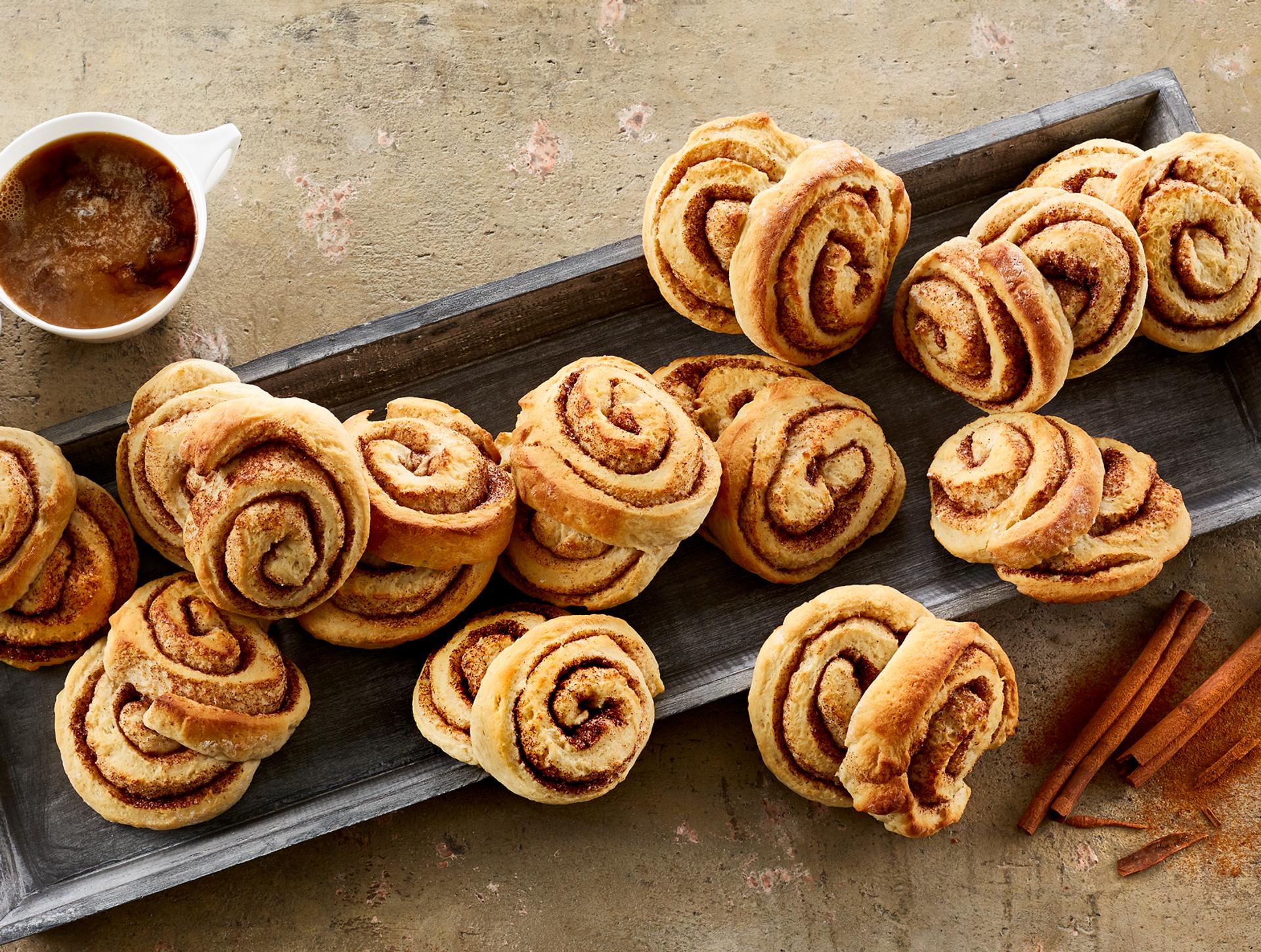 Kanelboller med kvarg på et fat ved siden av en kopp kaffe med melk