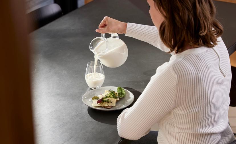 a woman is pouring milk into a glass while sitting at a table .