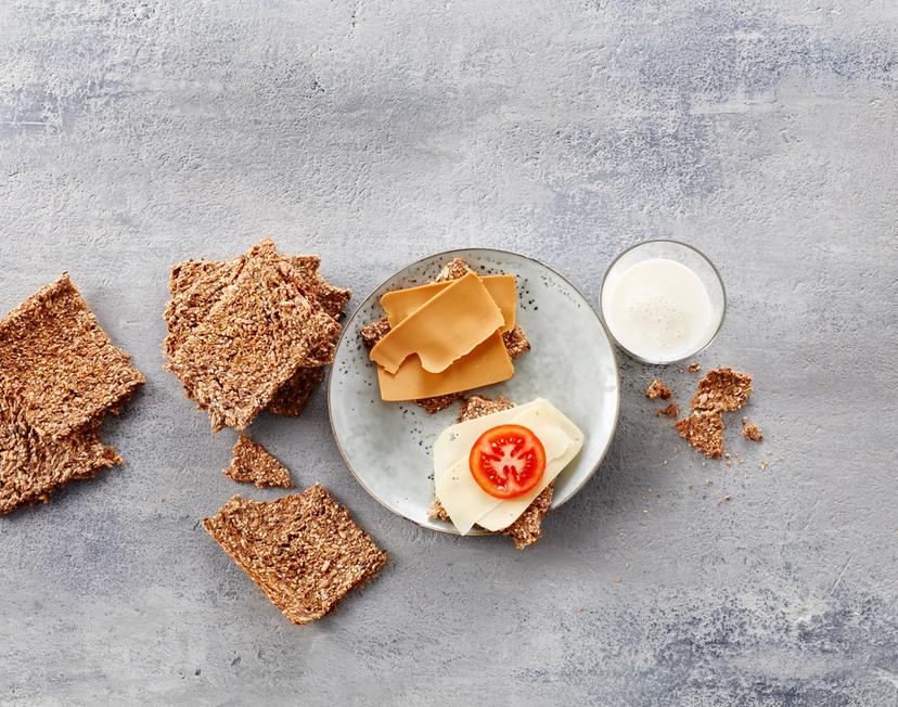Hjemmelaget knekkebrød med gulost og brunost ved siden av et glass melk