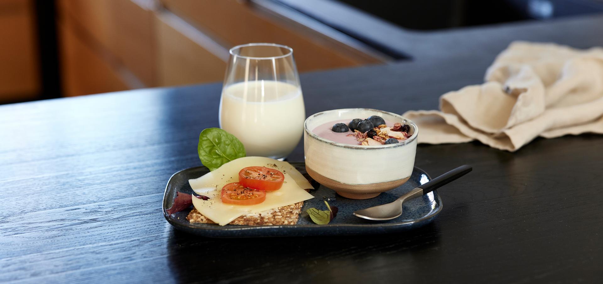 Knekkebrød med gulost og reddik, et glass melk og en skål yoghurt med bær