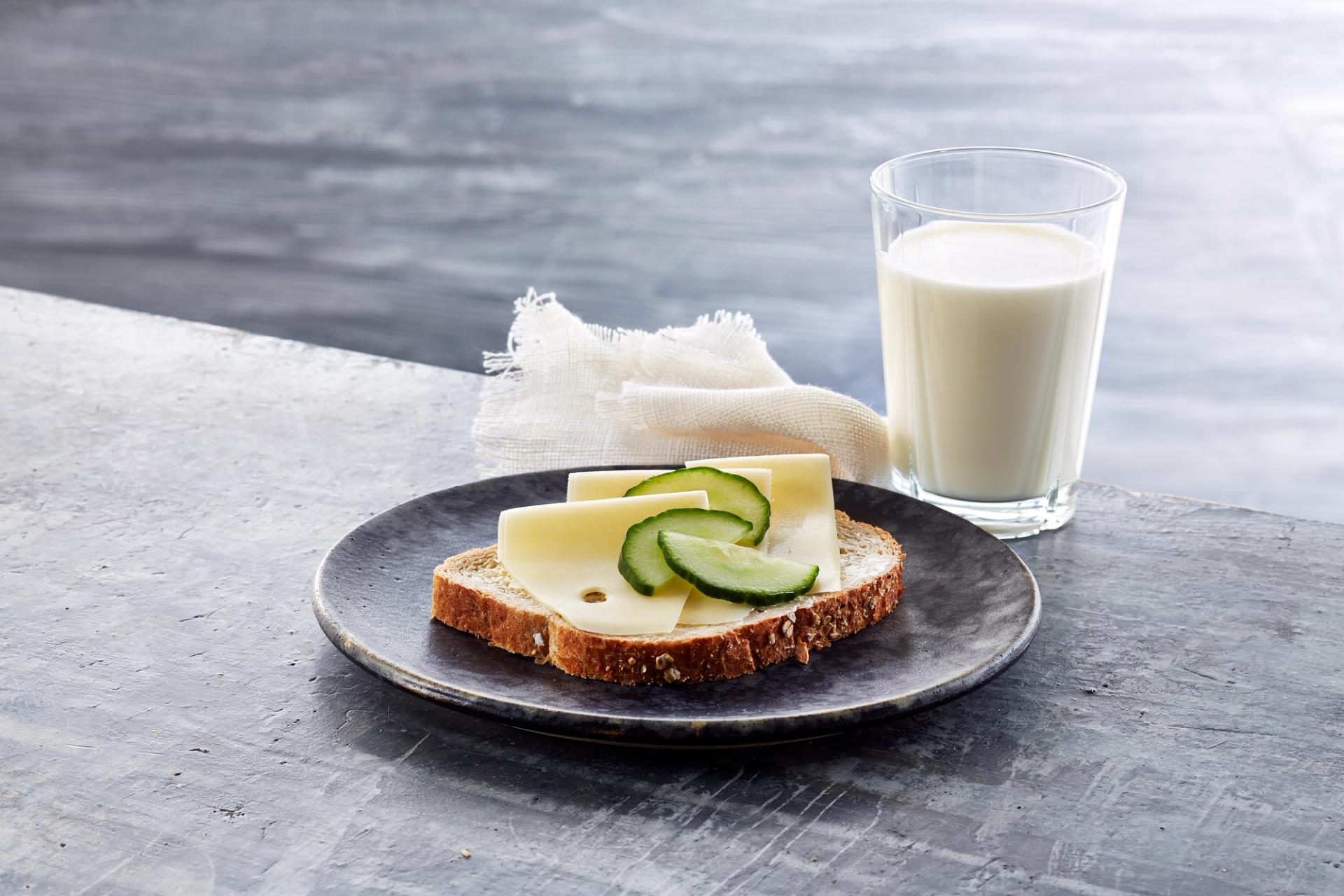 Brødskive med gulost og agurk og et glass melk.