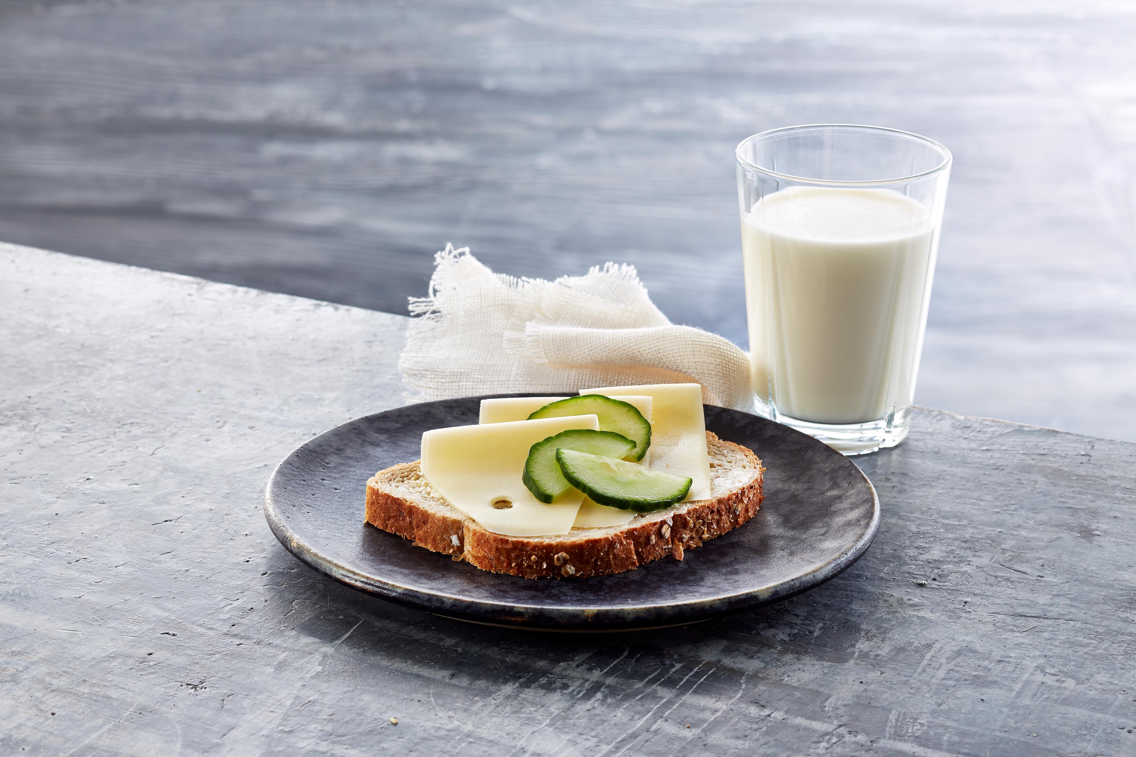 Brødskive med gulost og agurk og et glass melk.