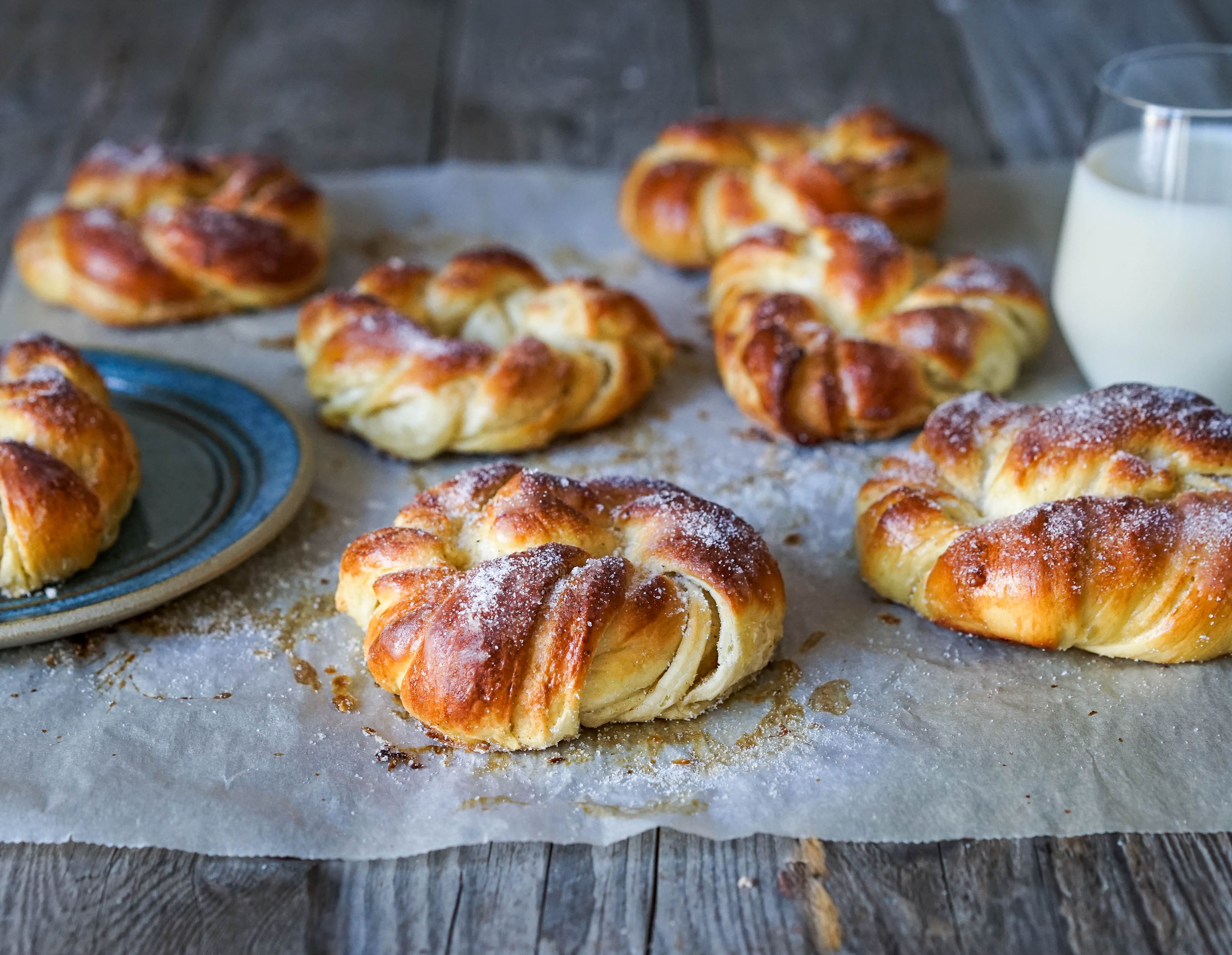 Kardemommeboller med melisdryss på et bakepapir med et glass melk ved siden av