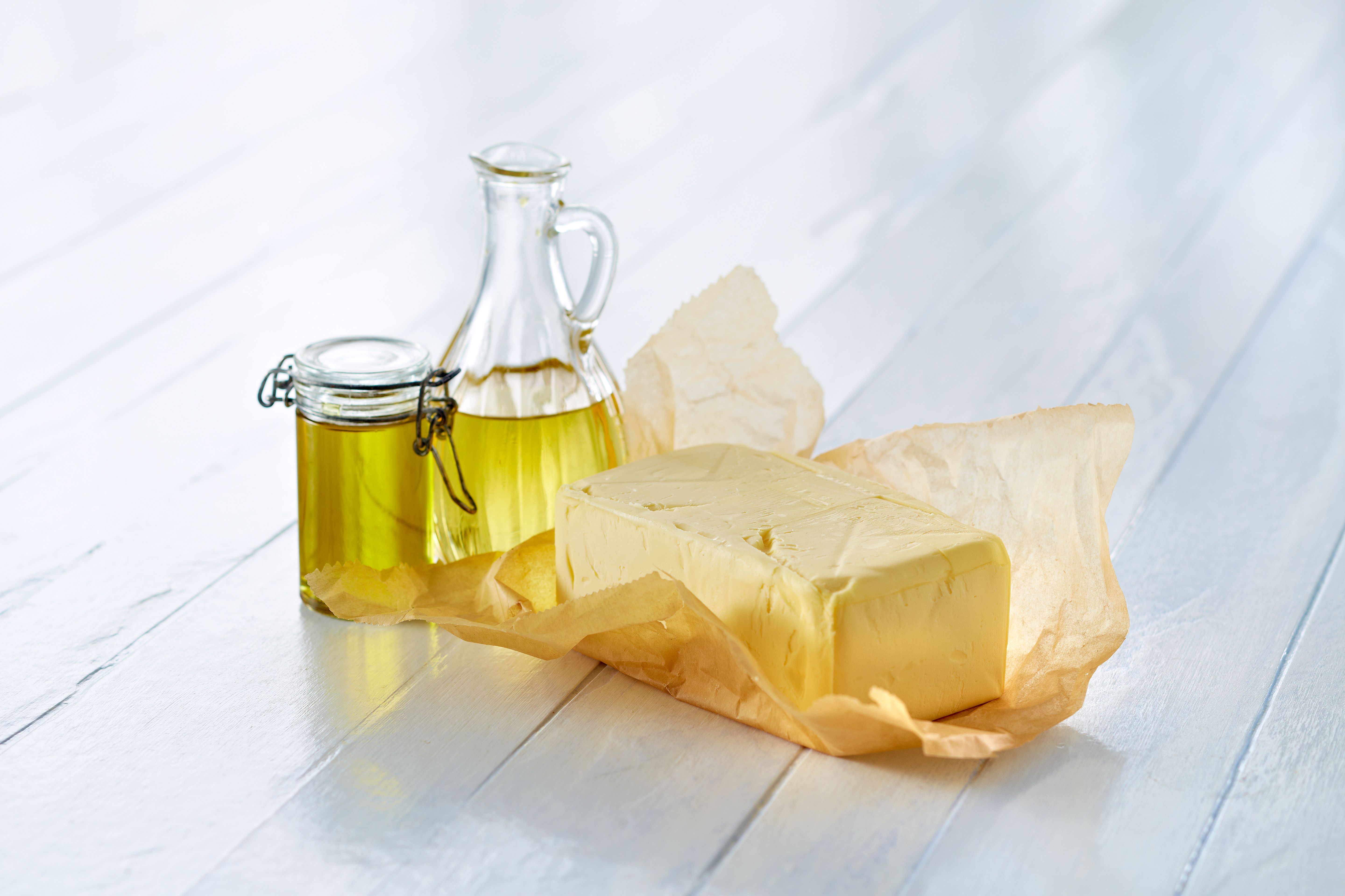 En krukke med olje og en smørblokk på et hvitt bord.