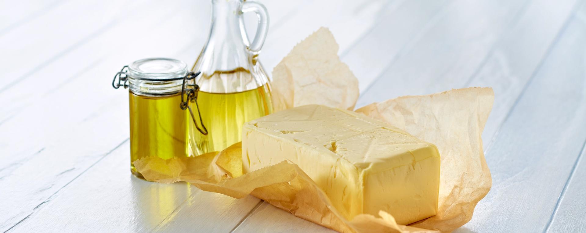 En krukke med olje og en smørblokk på et hvitt bord.