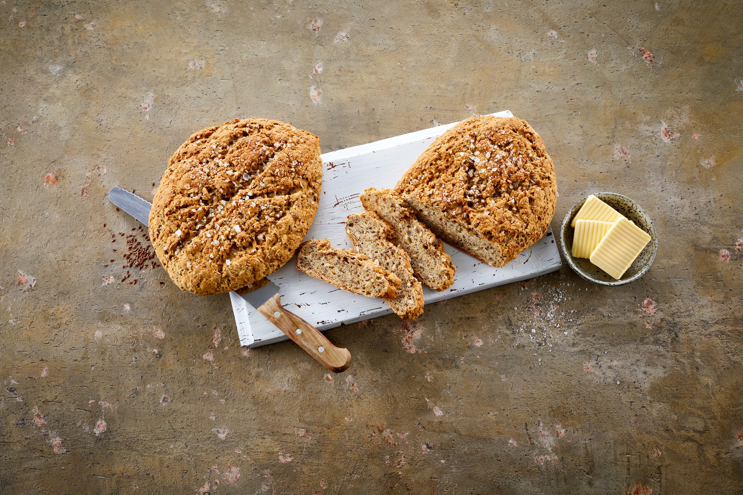 To runde brød med syrnet melk på en fjøl ved siden av en skål med smør i skiver.