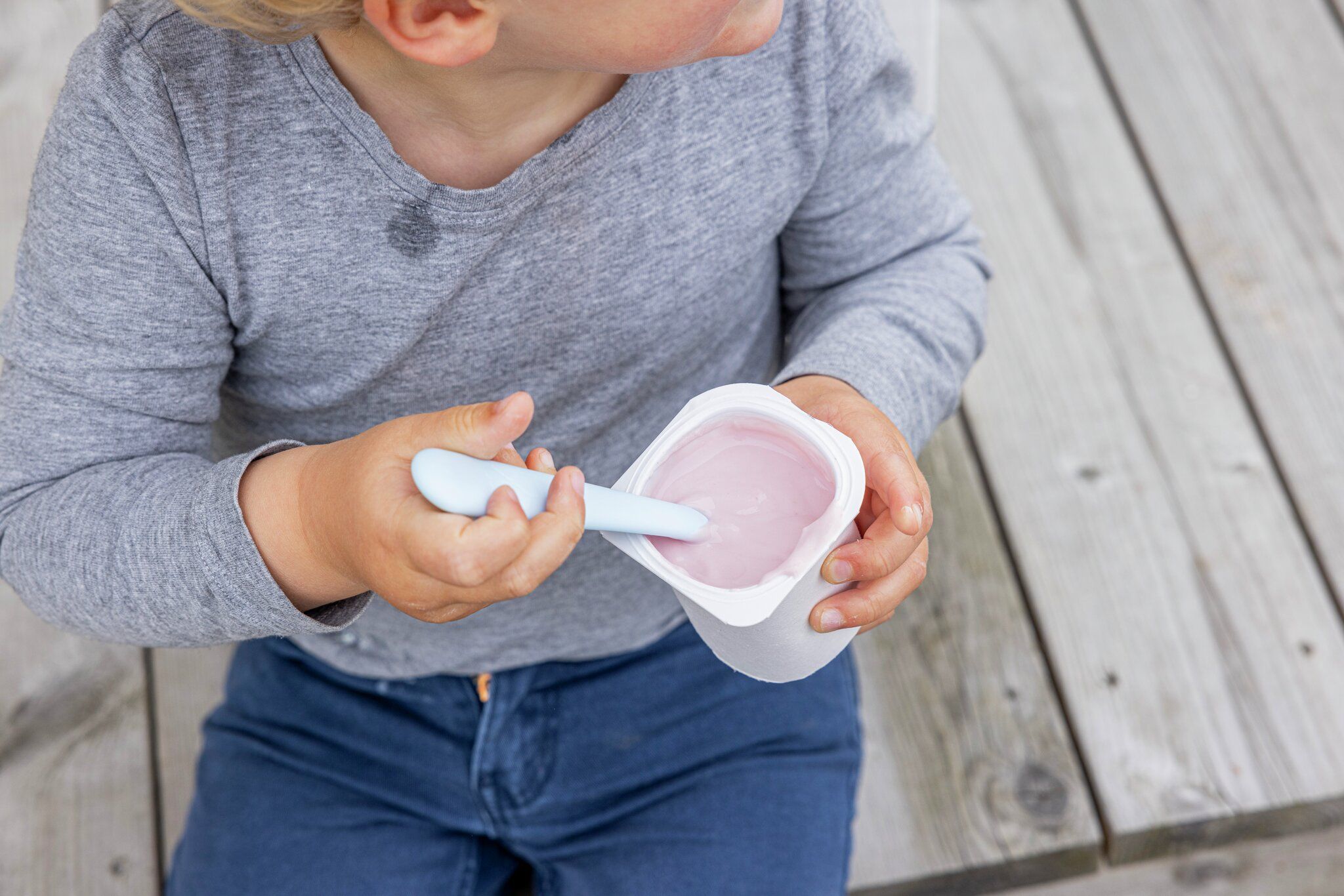 Child eating pink yogurt with a spoon.