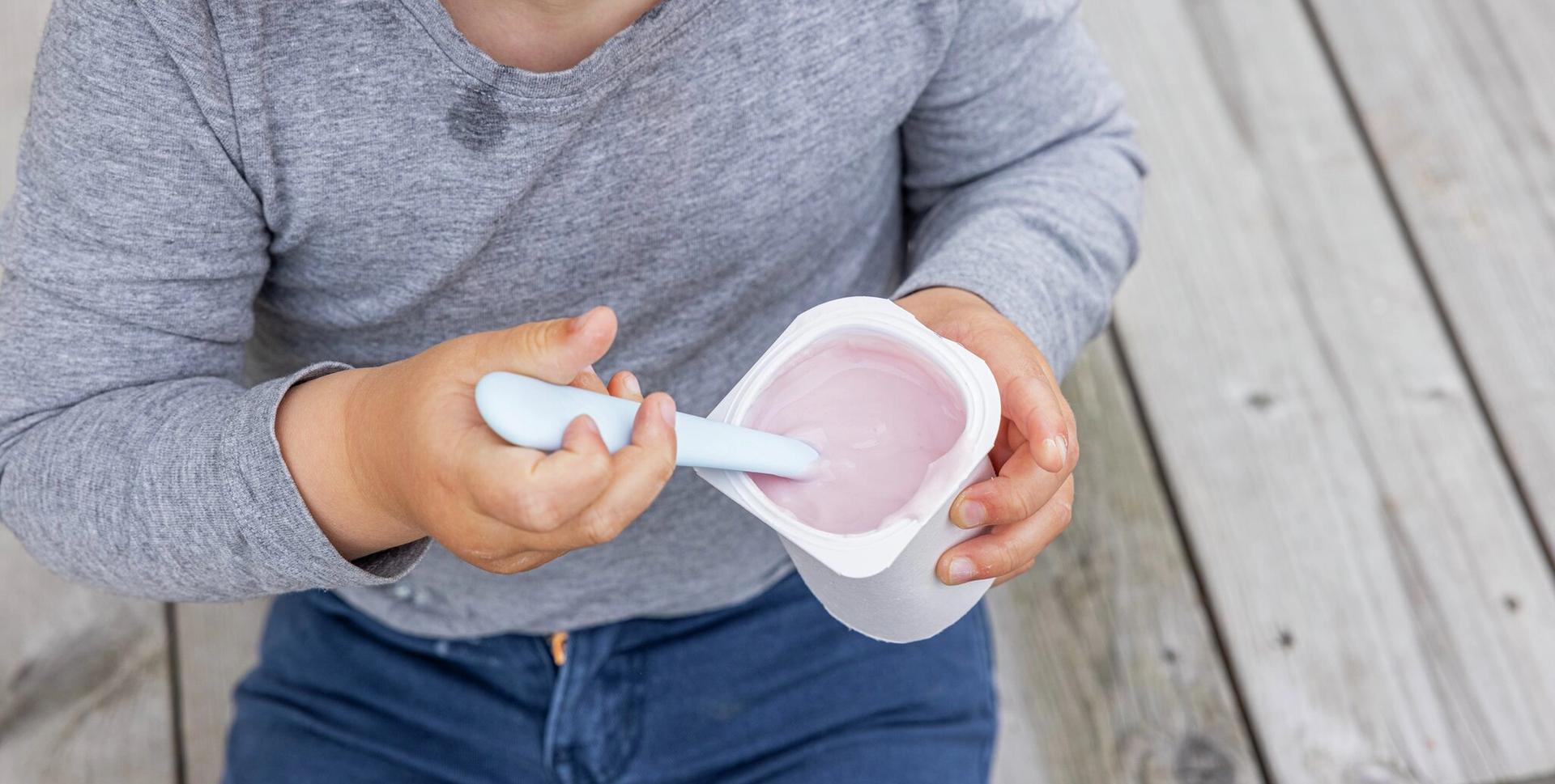 Child eating pink yogurt with a spoon.