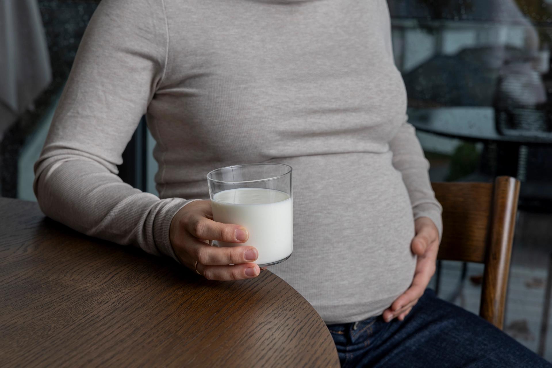 Pregnant woman holding a glass of milk and touching her belly.