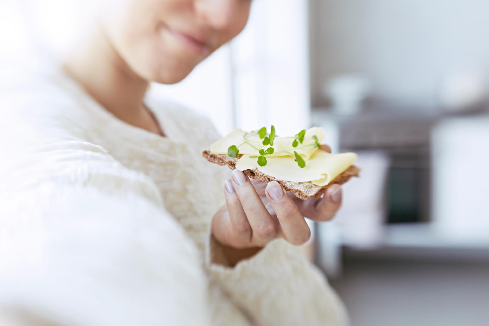 Dame som spiser knekkebrød med ost og urter.