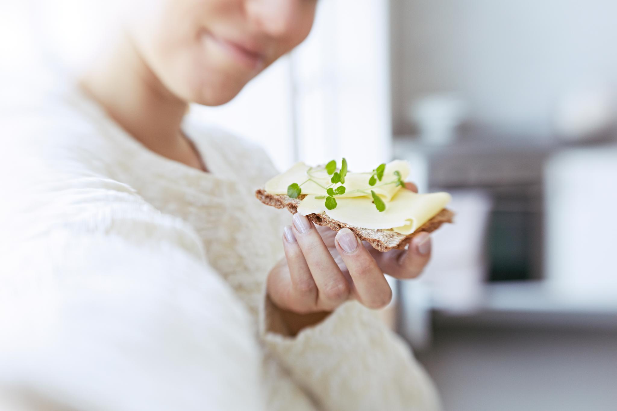 Dame som spiser knekkebrød med ost og urter.