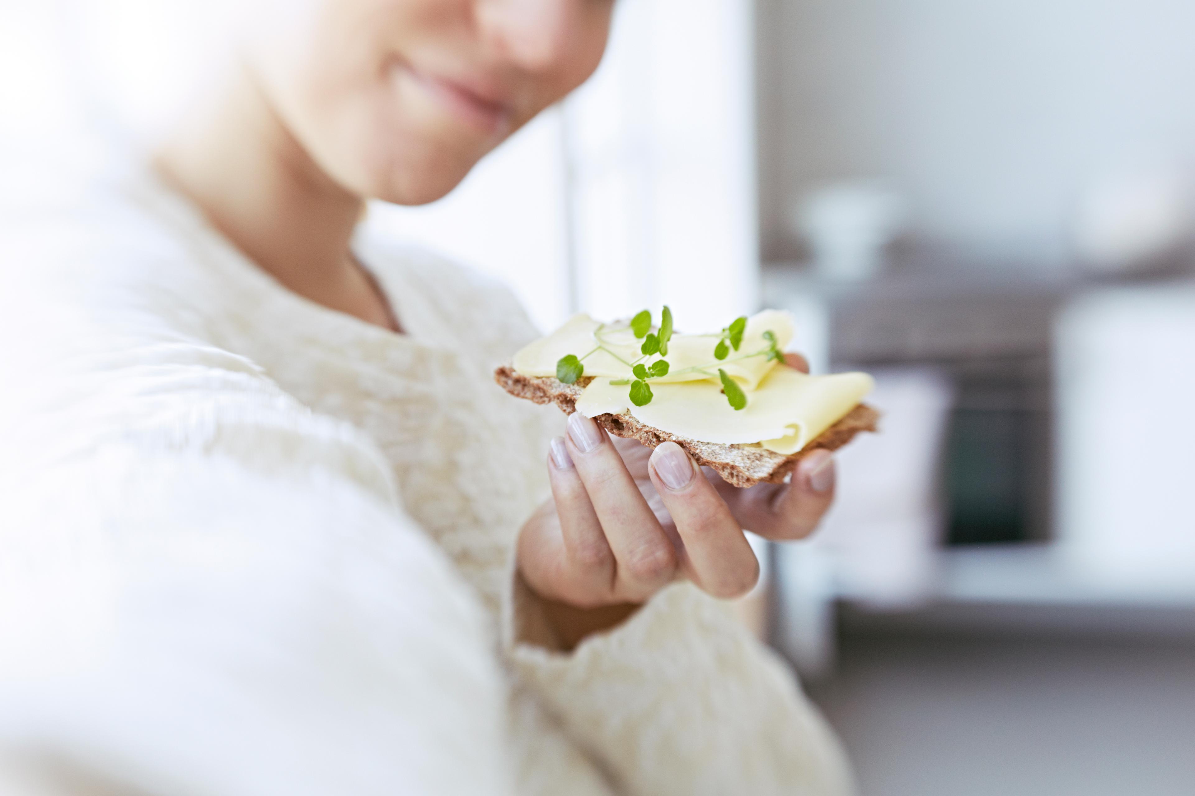 Dame som spiser knekkebrød med ost og urter.