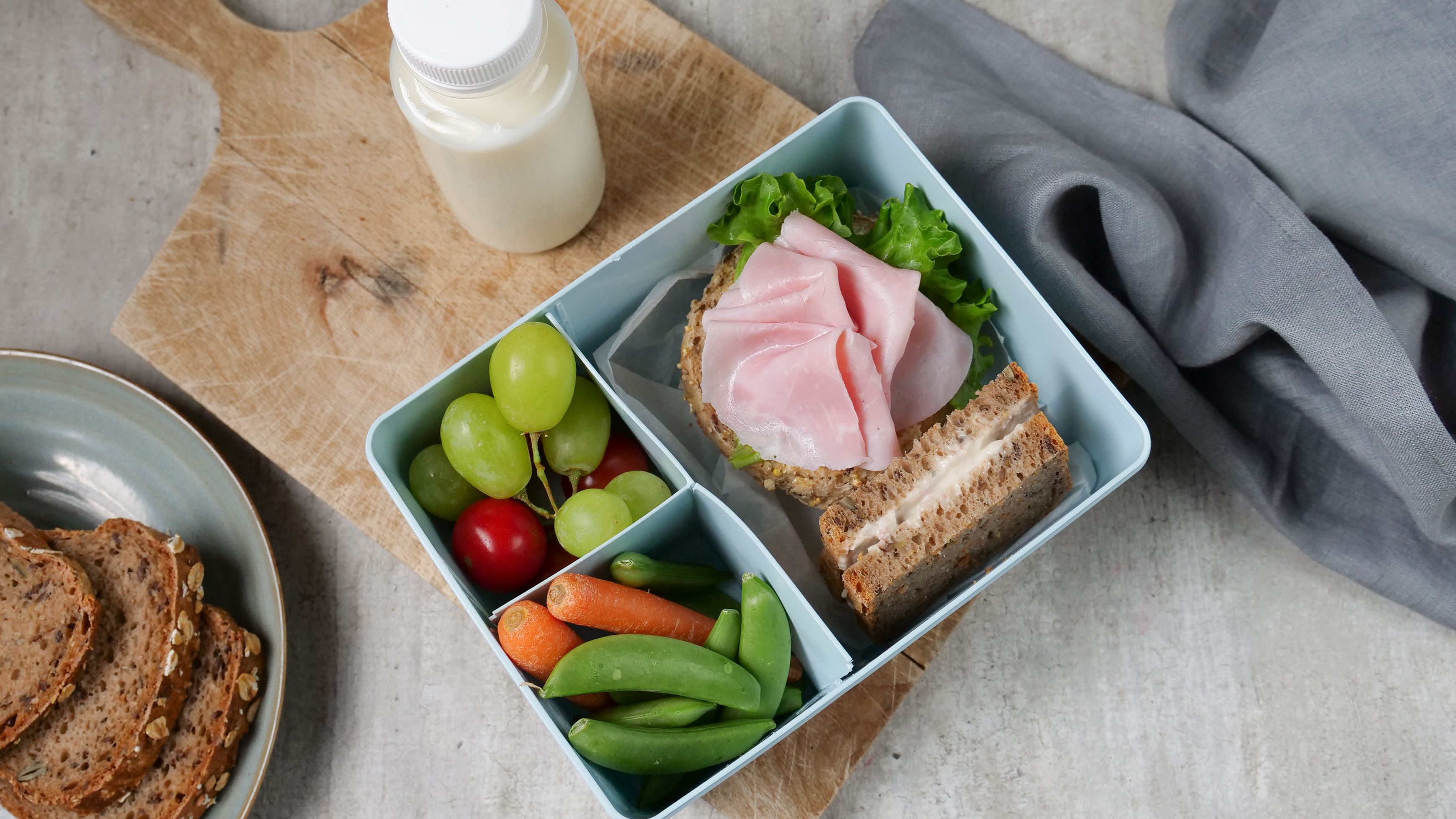 a lunch box filled with sandwiches , fruit , vegetables and a bottle of milk .