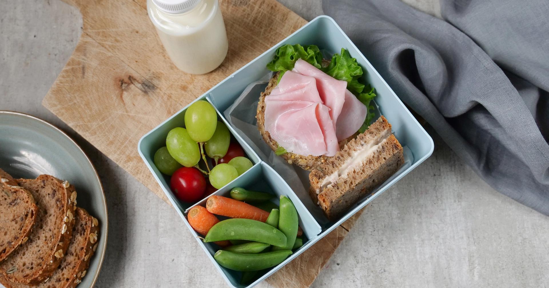 a lunch box filled with sandwiches , fruit , vegetables and a bottle of milk .