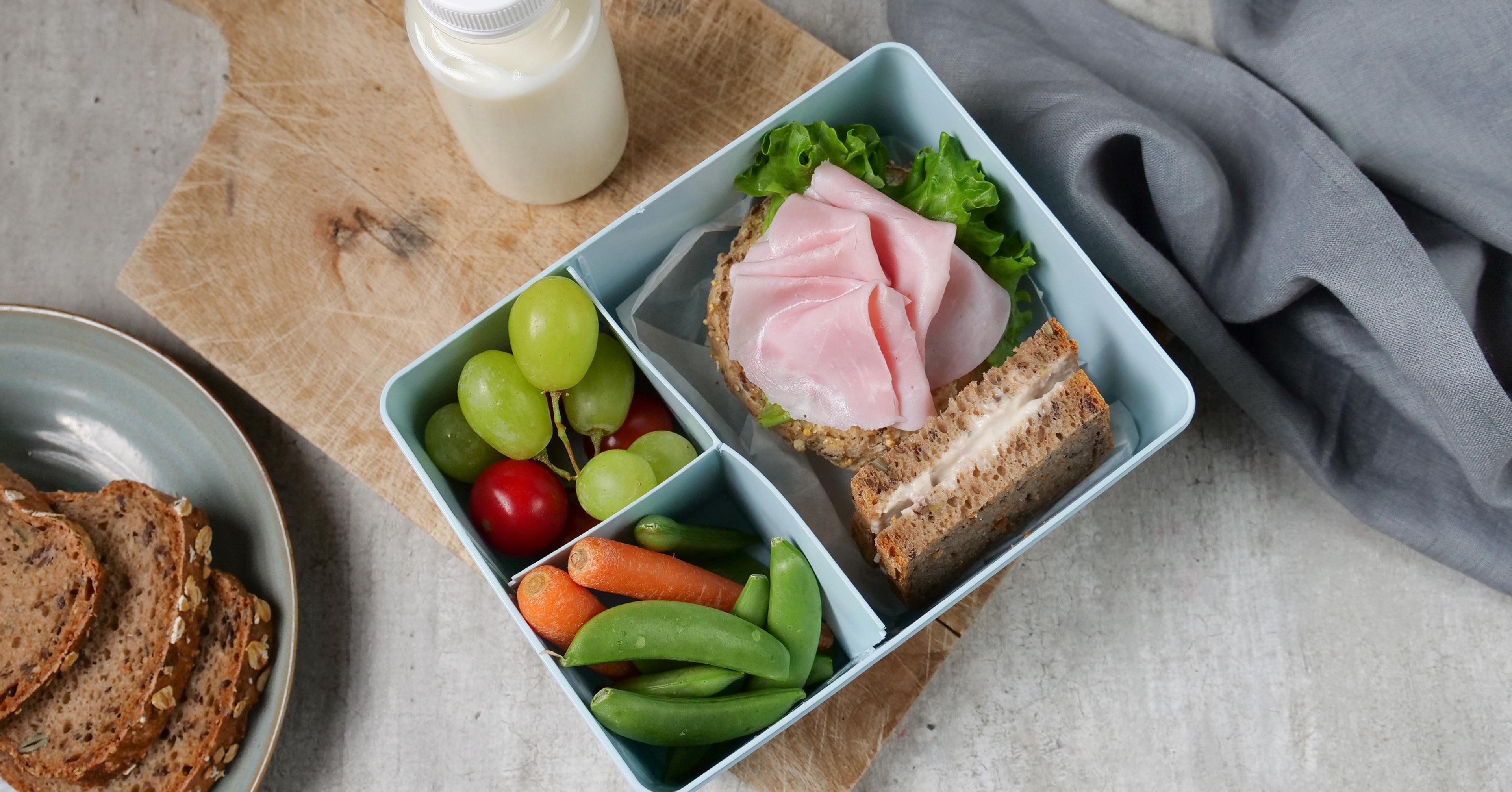 a lunch box filled with sandwiches , fruit , vegetables and a bottle of milk .