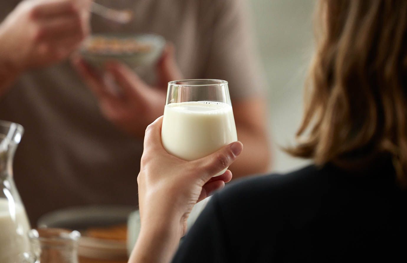 a woman is holding a glass of milk while a man is eating cereal .
