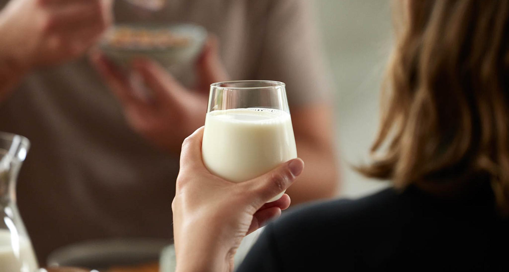 a woman is holding a glass of milk while a man is eating cereal .