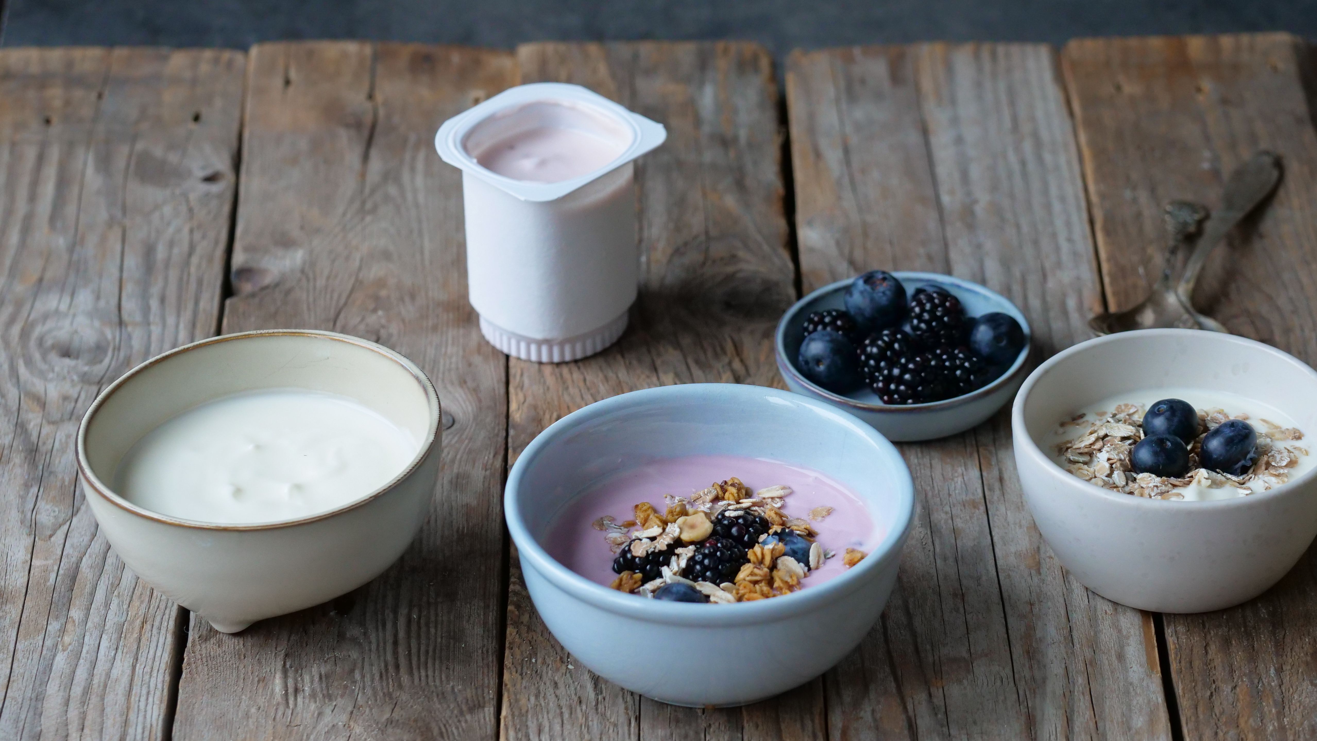 Different bowls of yogurt with fruit, granola, and oats on a wooden table.