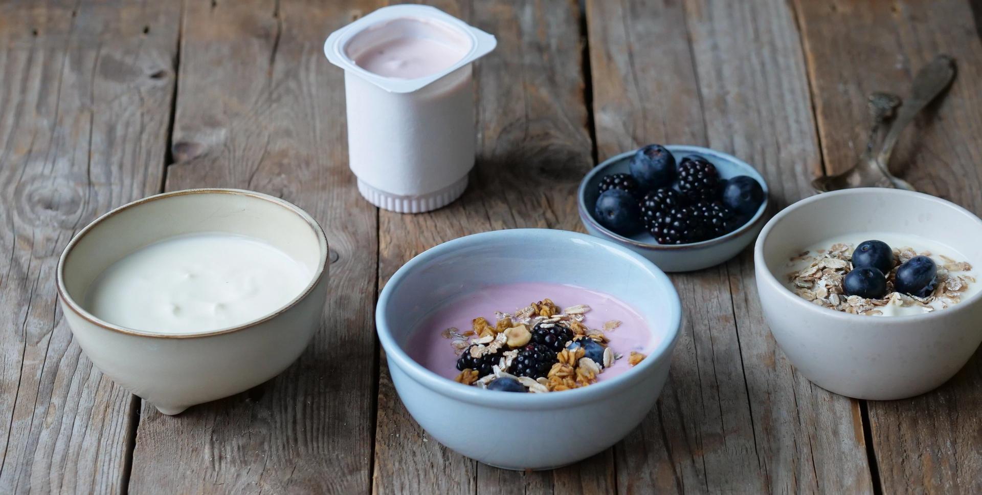 Different bowls of yogurt with fruit, granola, and oats on a wooden table.