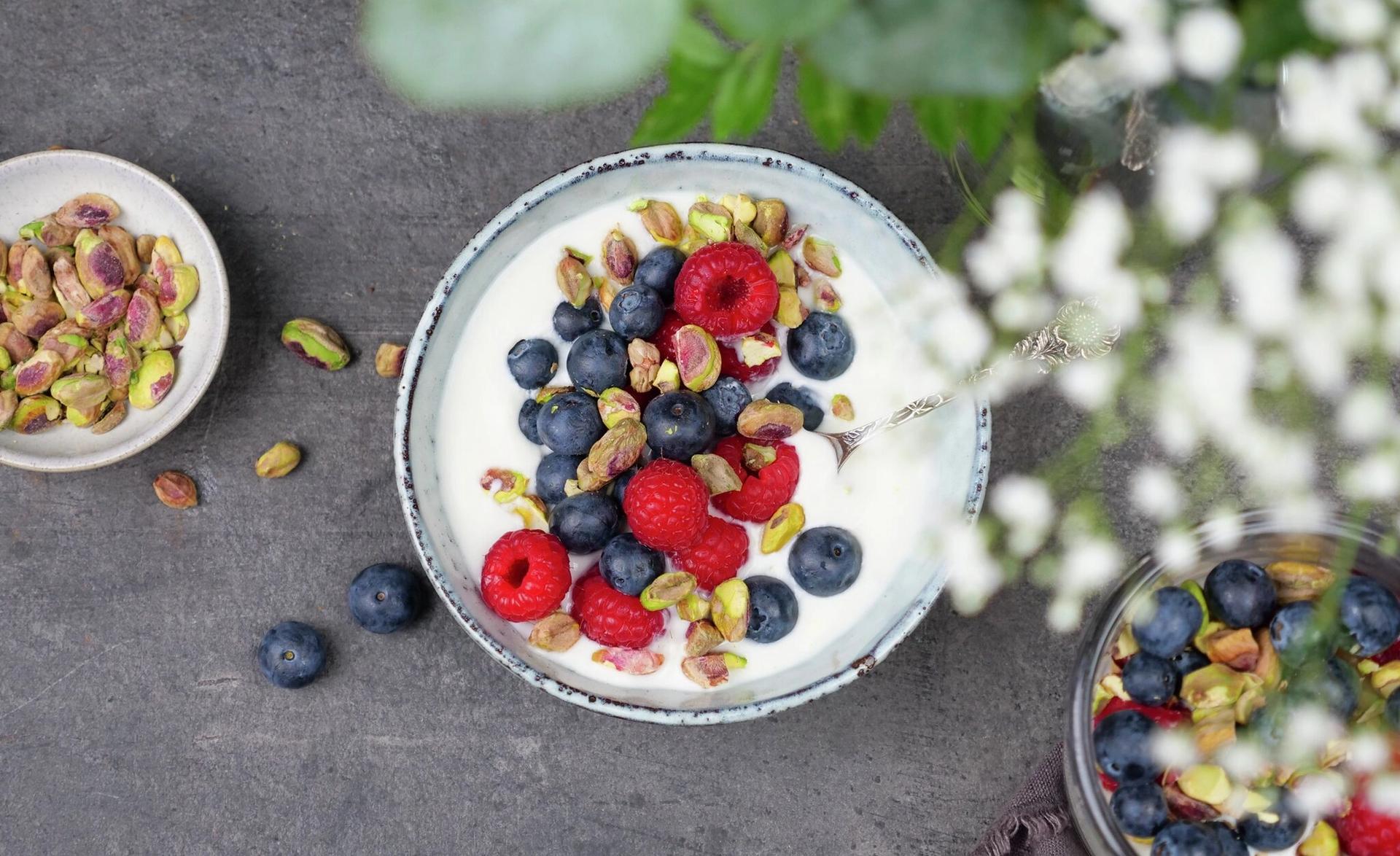 En skål med yoghurt toppet med blåbær, bringebær og pistasjenøtter