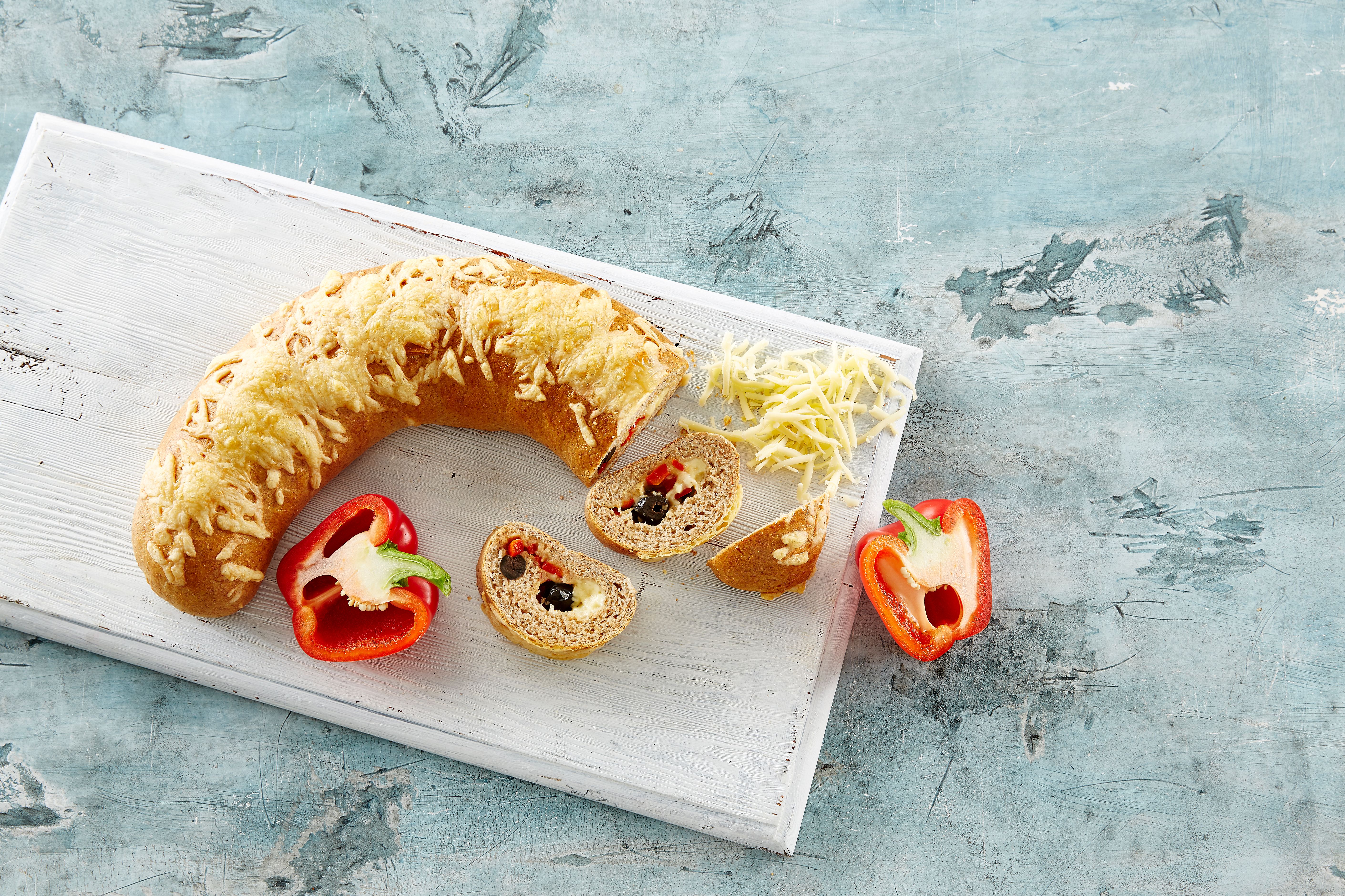 Brød med ost og oliven på en fjøl ved siden av to halve paprika