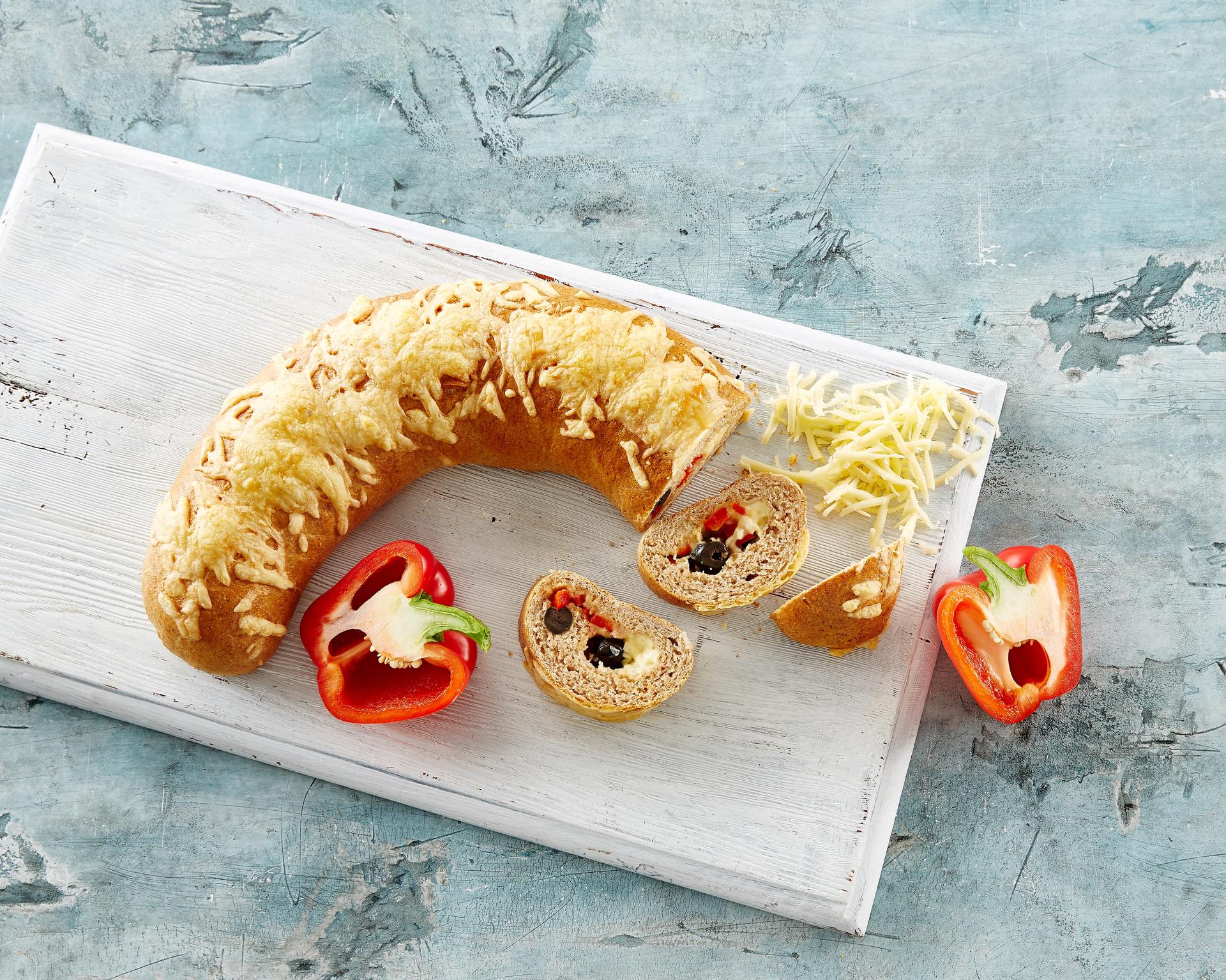 Brød med ost og oliven på en fjøl ved siden av to halve paprika