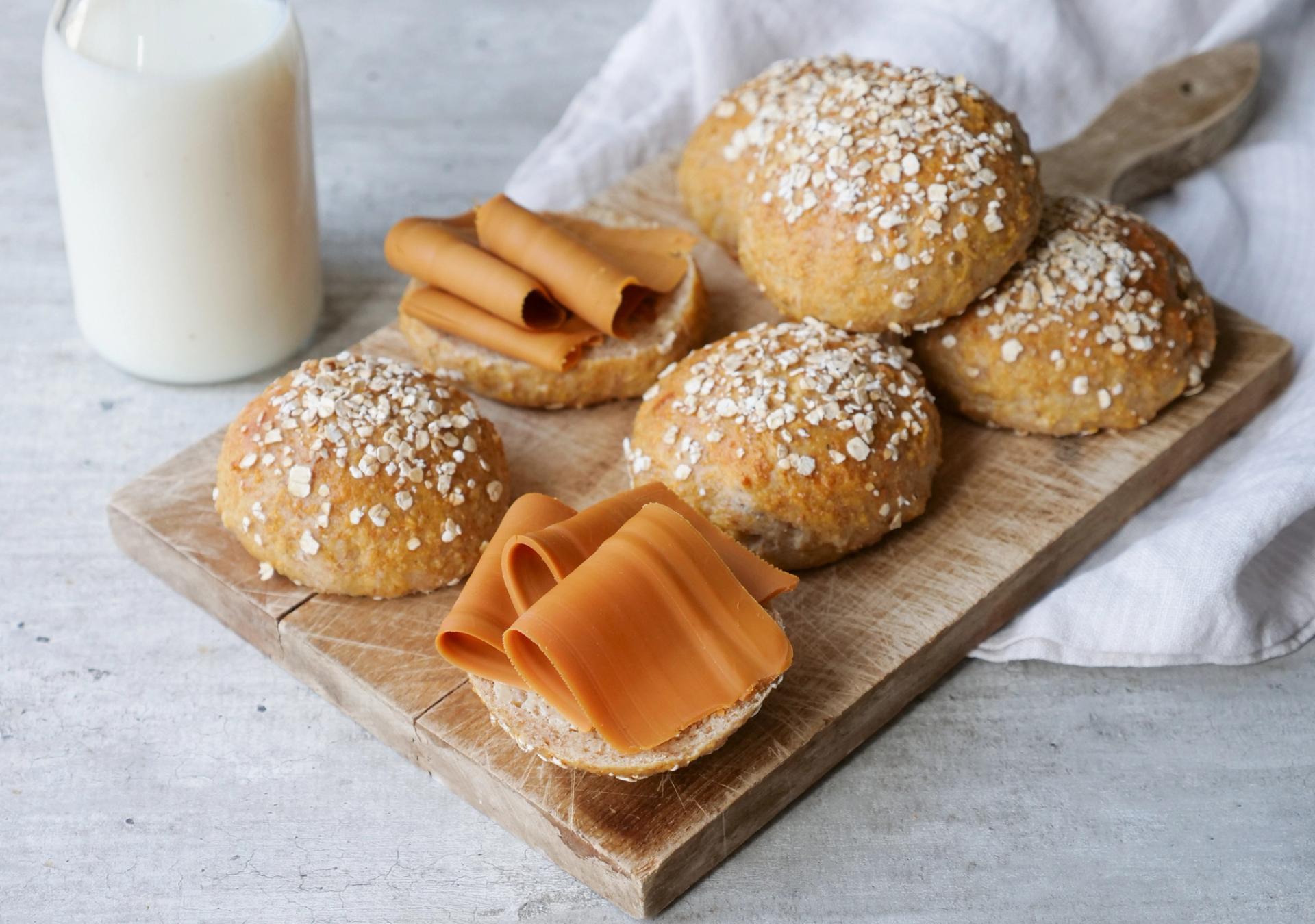 a wooden cutting board topped with buns , cheese and a glass of milk .