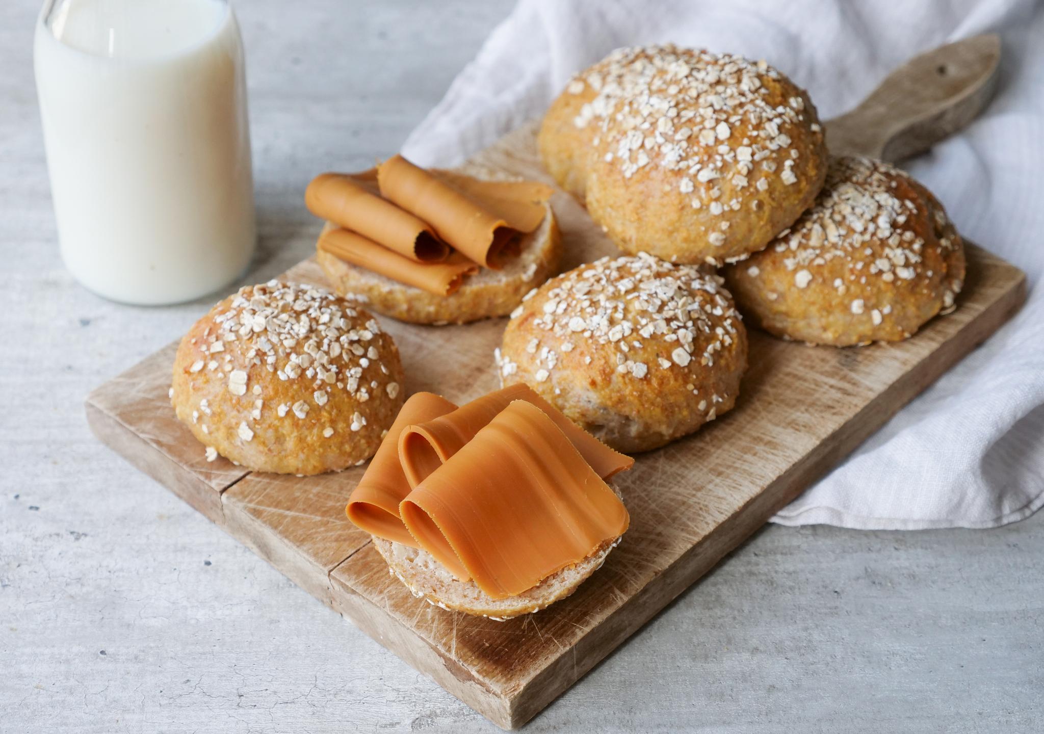 a wooden cutting board topped with buns , cheese and a glass of milk .