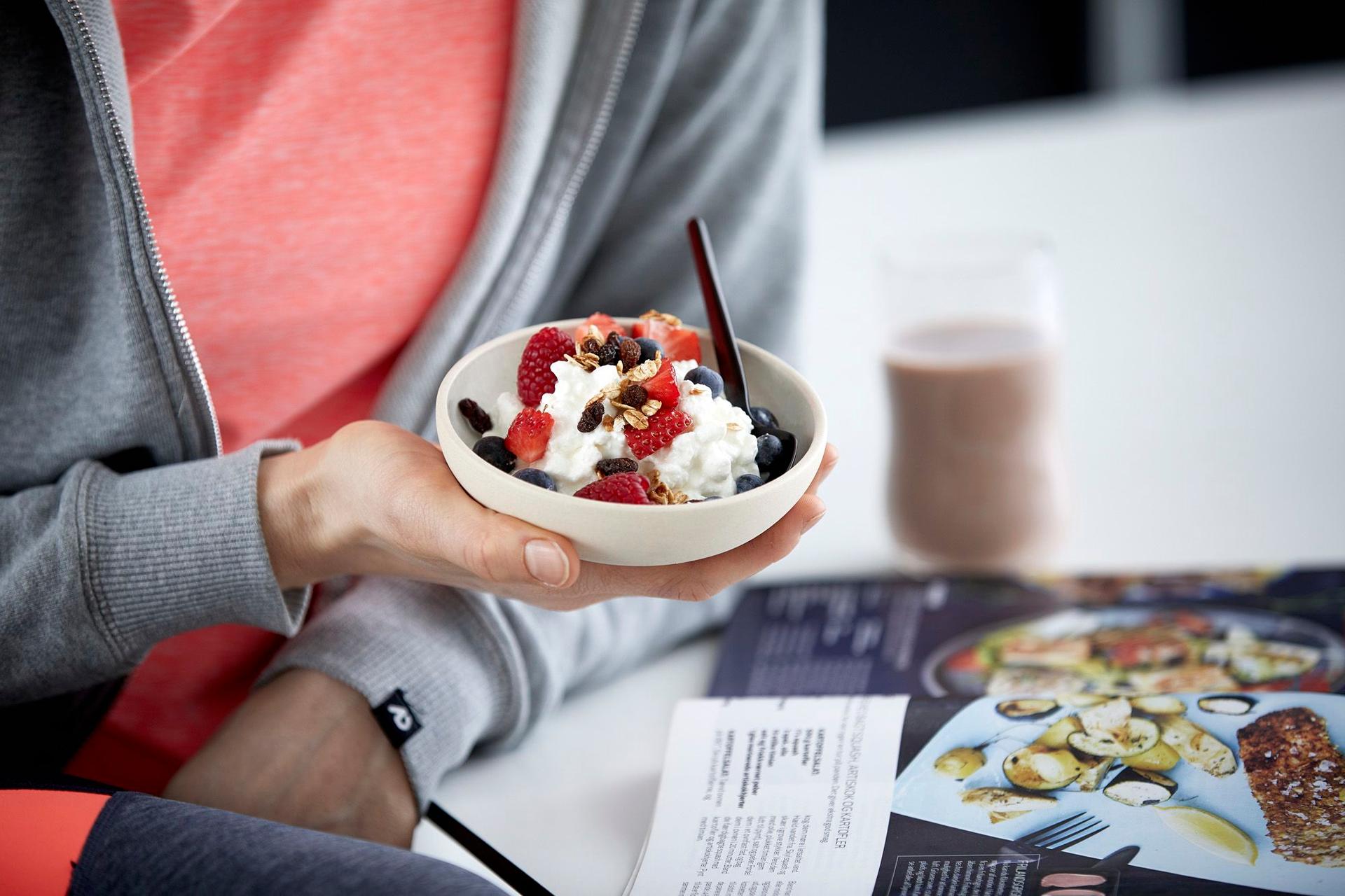 a person is holding a bowl of cottage cheese and fruit while reading a magazine .