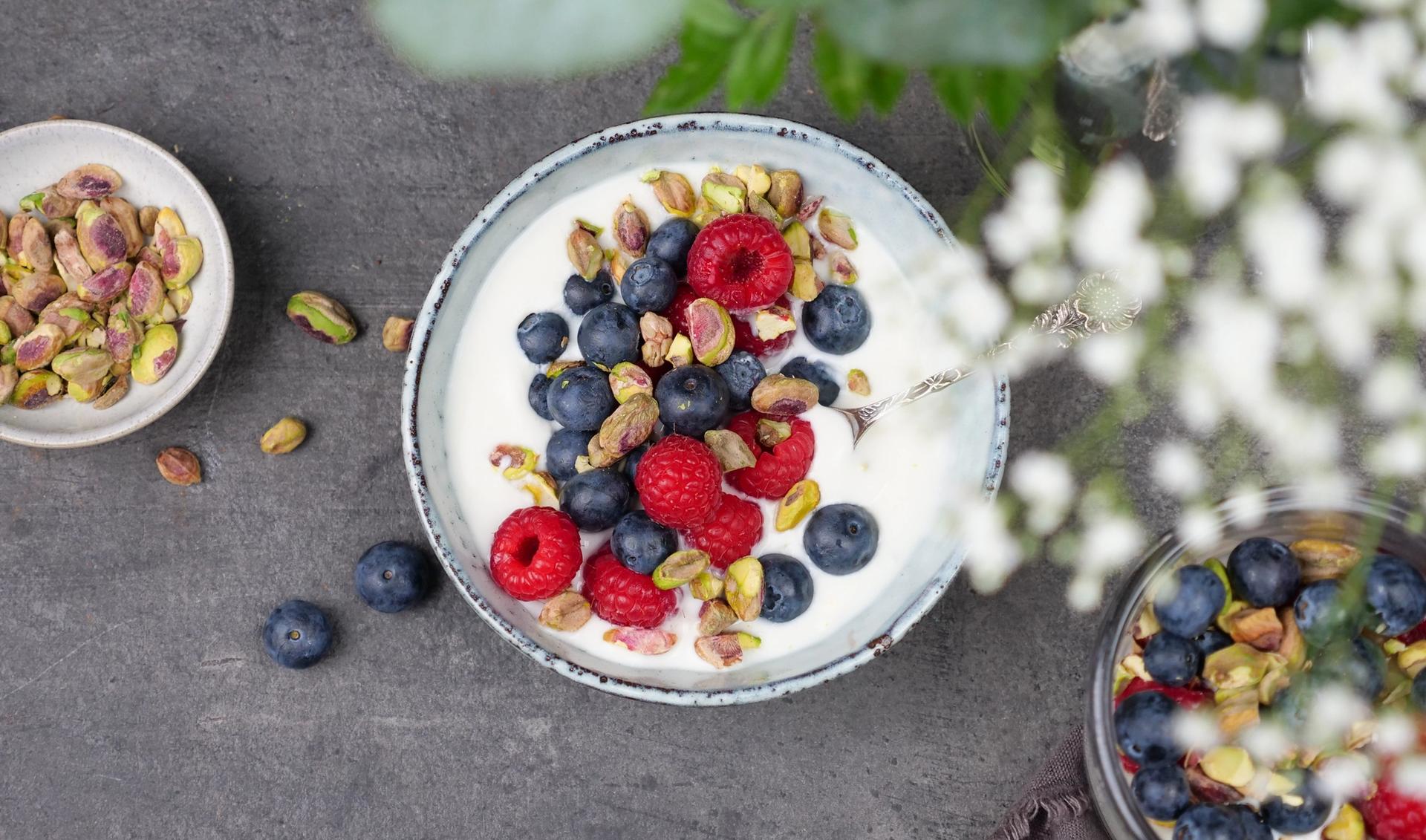 En skål med yoghurt toppet med blåbær, bringebær og pistasjenøtter