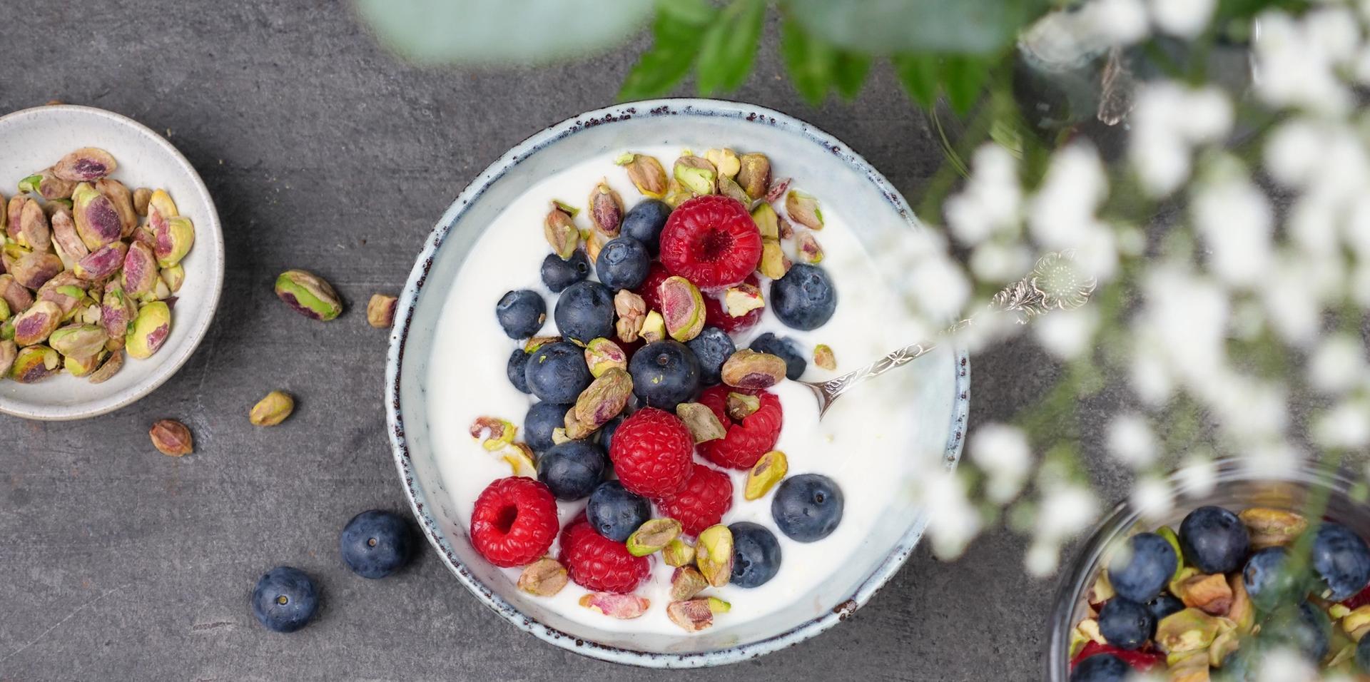 En skål med yoghurt toppet med blåbær, bringebær og pistasjenøtter