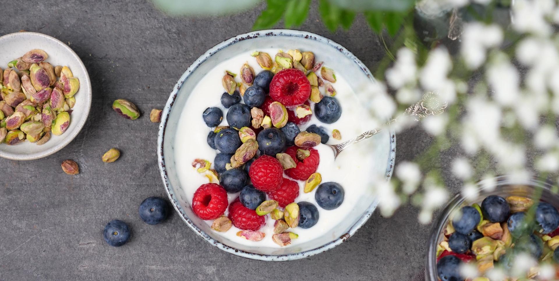 En skål med yoghurt toppet med blåbær, bringebær og pistasjenøtter