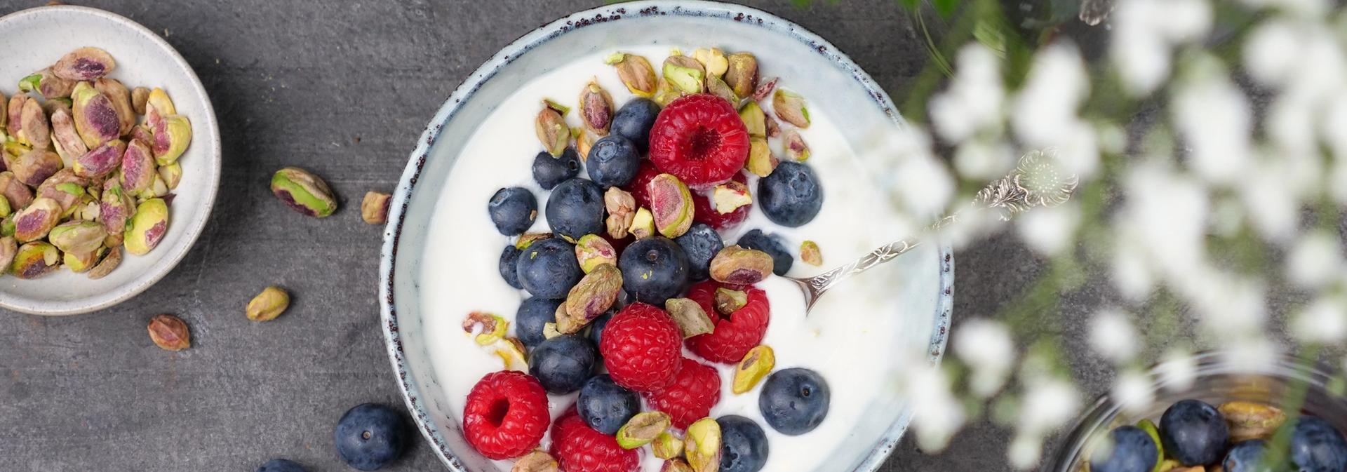 En skål med yoghurt toppet med blåbær, bringebær og pistasjenøtter