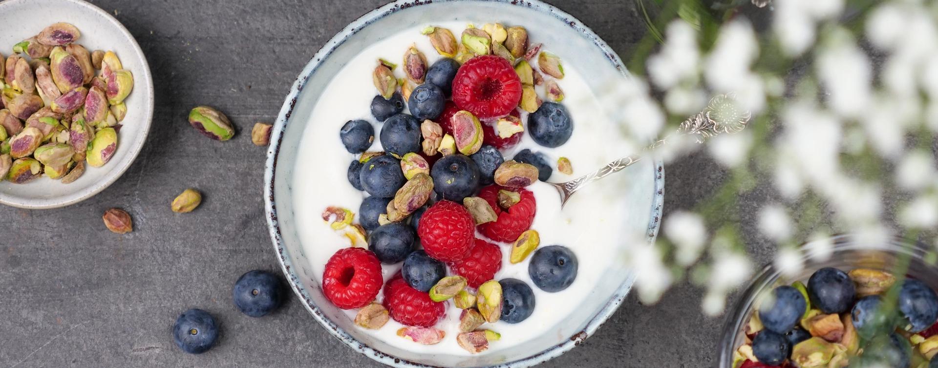 En skål med yoghurt toppet med blåbær, bringebær og pistasjenøtter