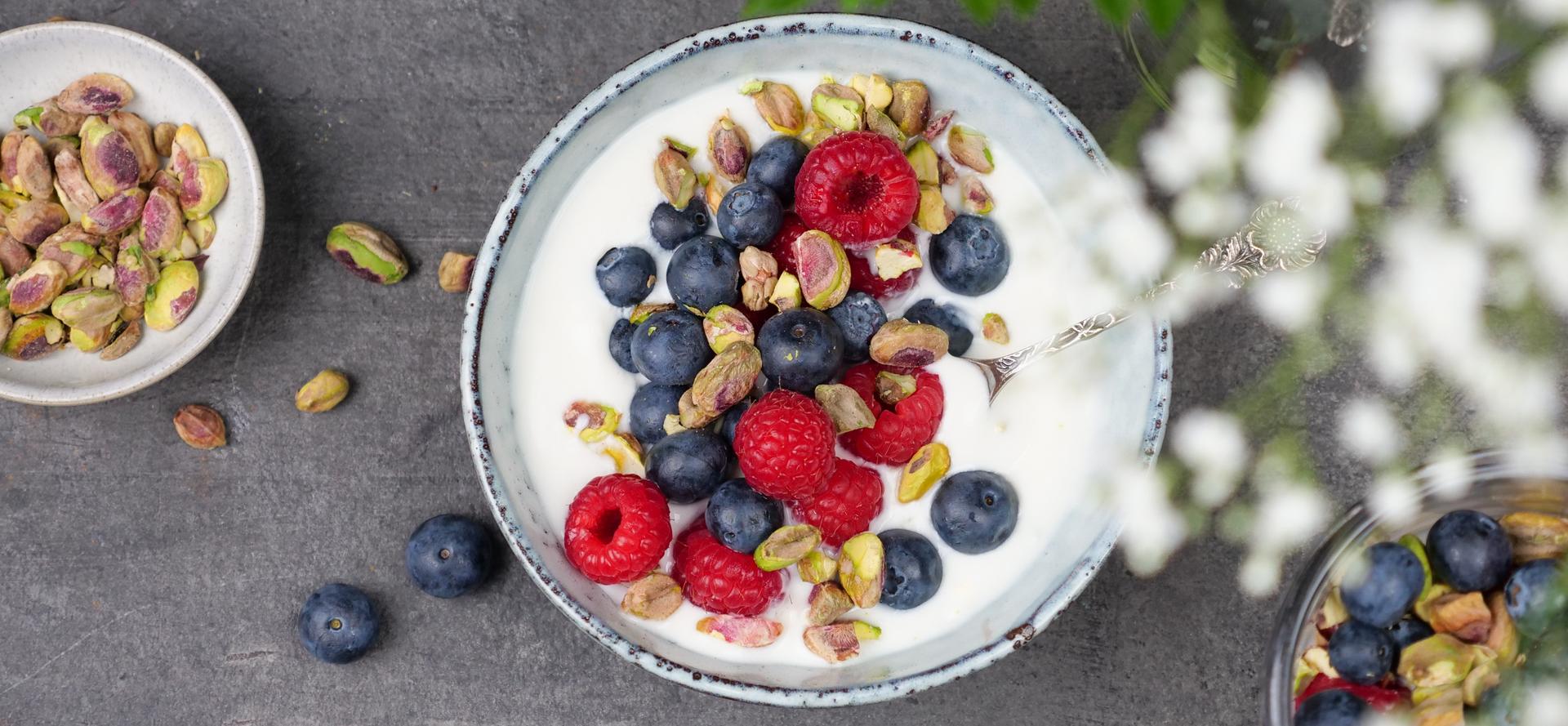 En skål med yoghurt toppet med blåbær, bringebær og pistasjenøtter