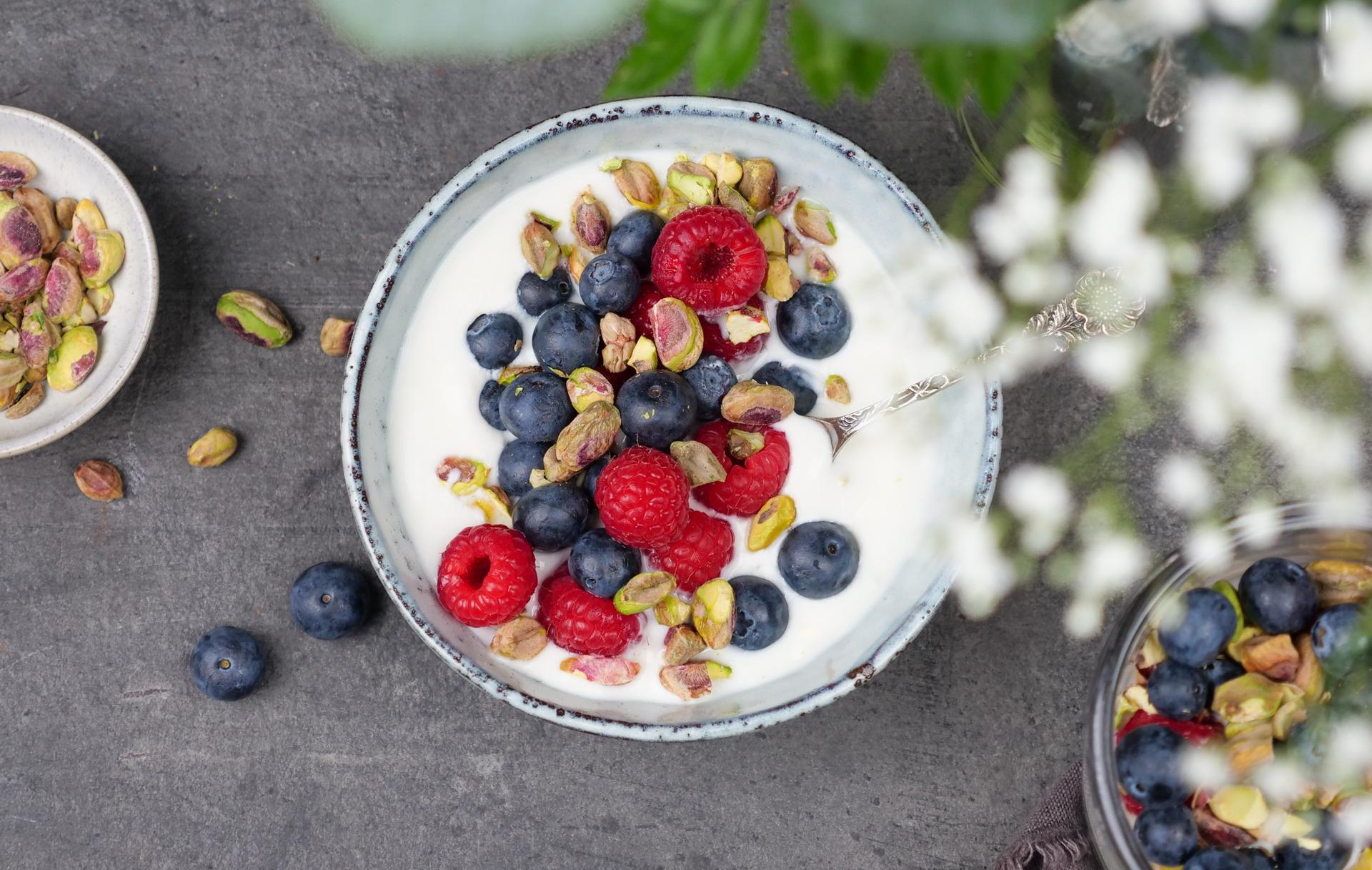 Skål med yoghurt, toppet med bringebær, blåbær og pistasjenøtter