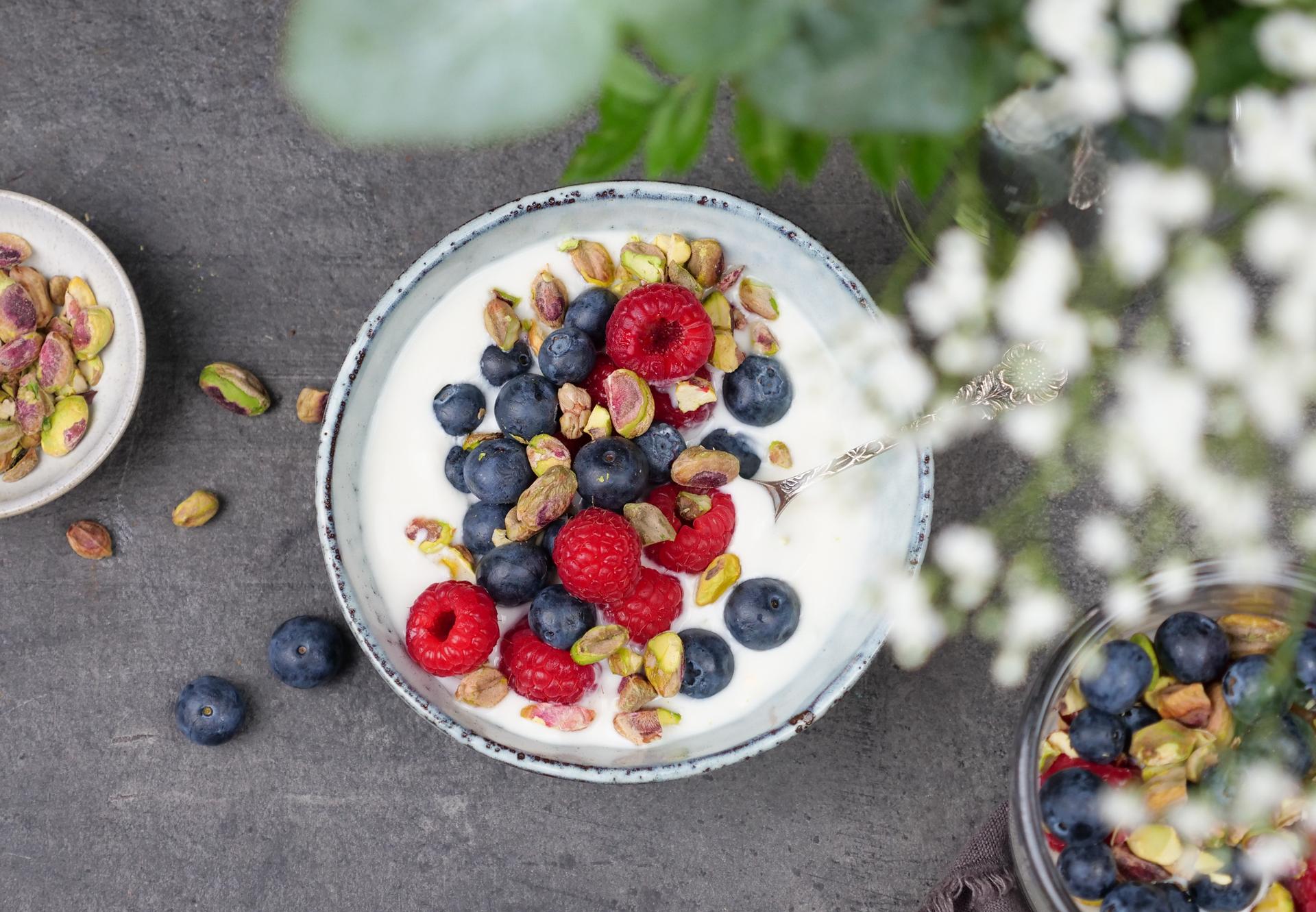 Dame og jente som sitter ved siden av hverandre i en sofa og smiler og spiser yoghurt.