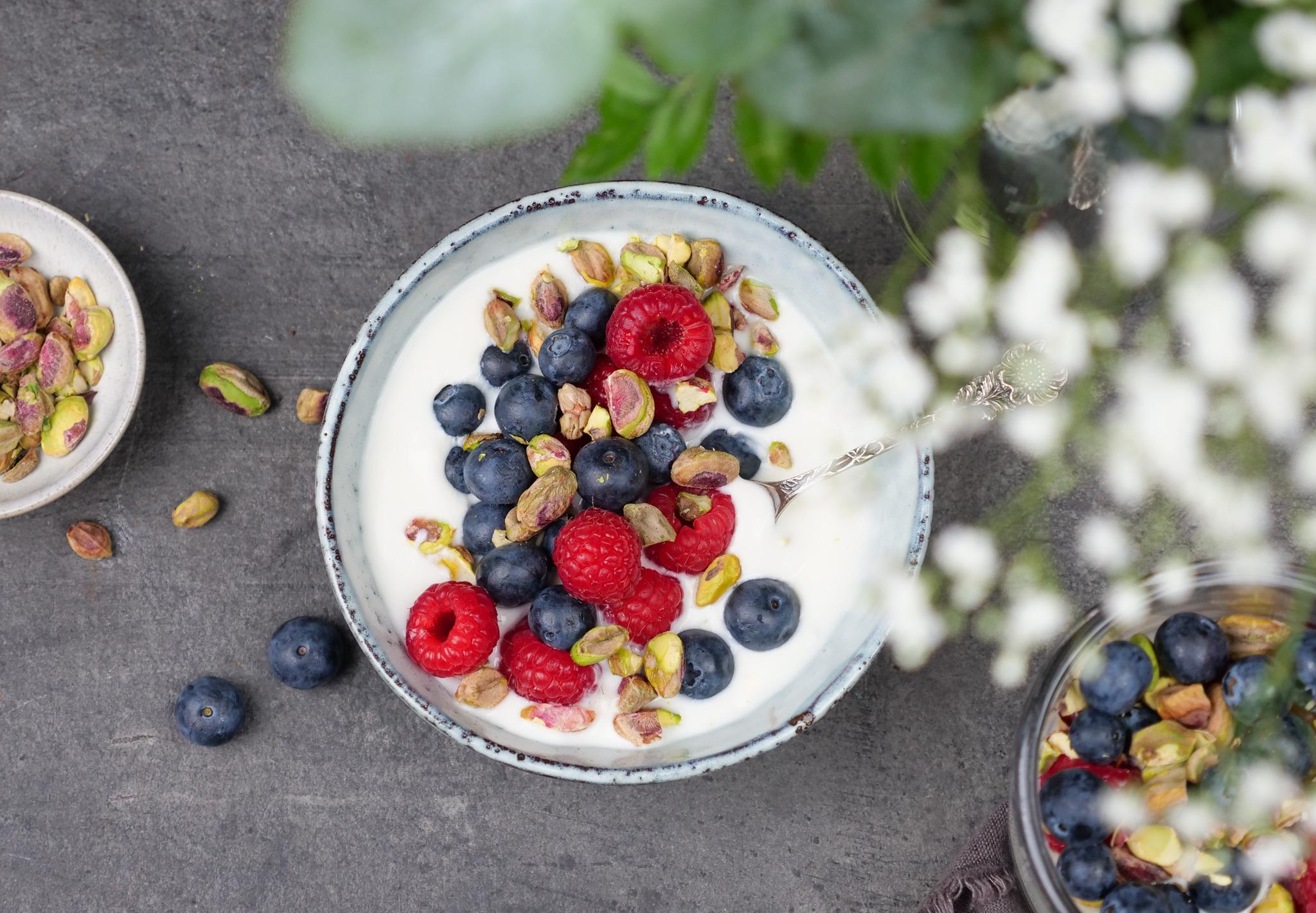 Dame og jente som sitter ved siden av hverandre i en sofa og smiler og spiser yoghurt.